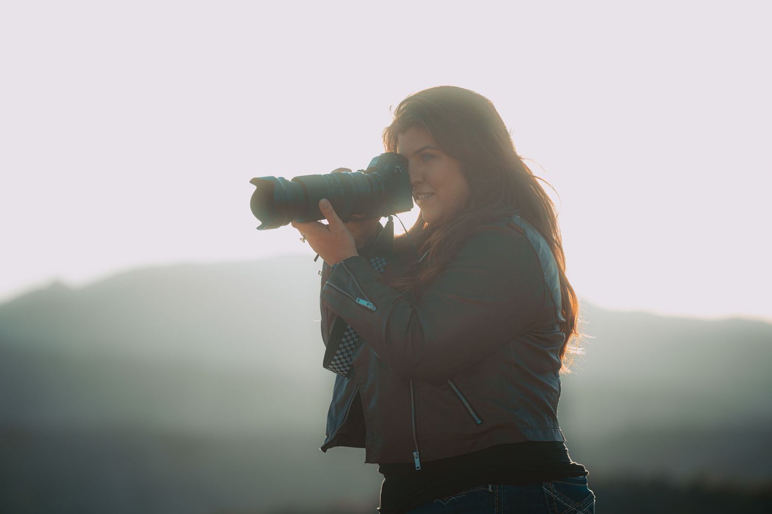 Female photographer shooting with telephoto lens in misty mountain landscape.