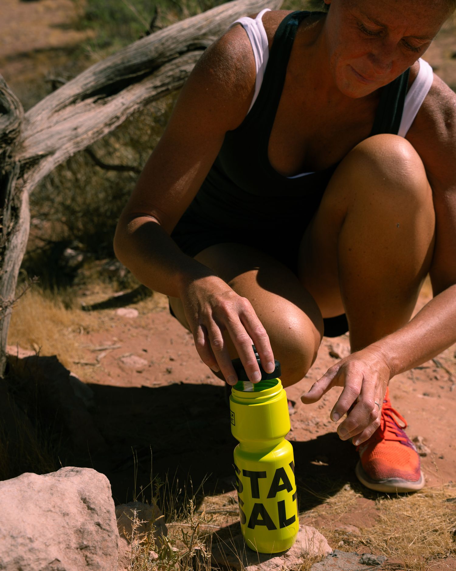 Athletic woman kneeling on desert trail preparing yellow LMNT electrolyte drink bottle outdoors.