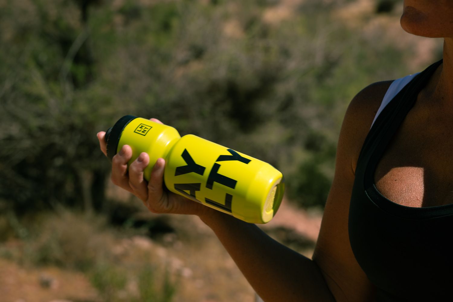 Close-up of woman holding yellow LMNT branded water bottle during outdoor trail run in nature.