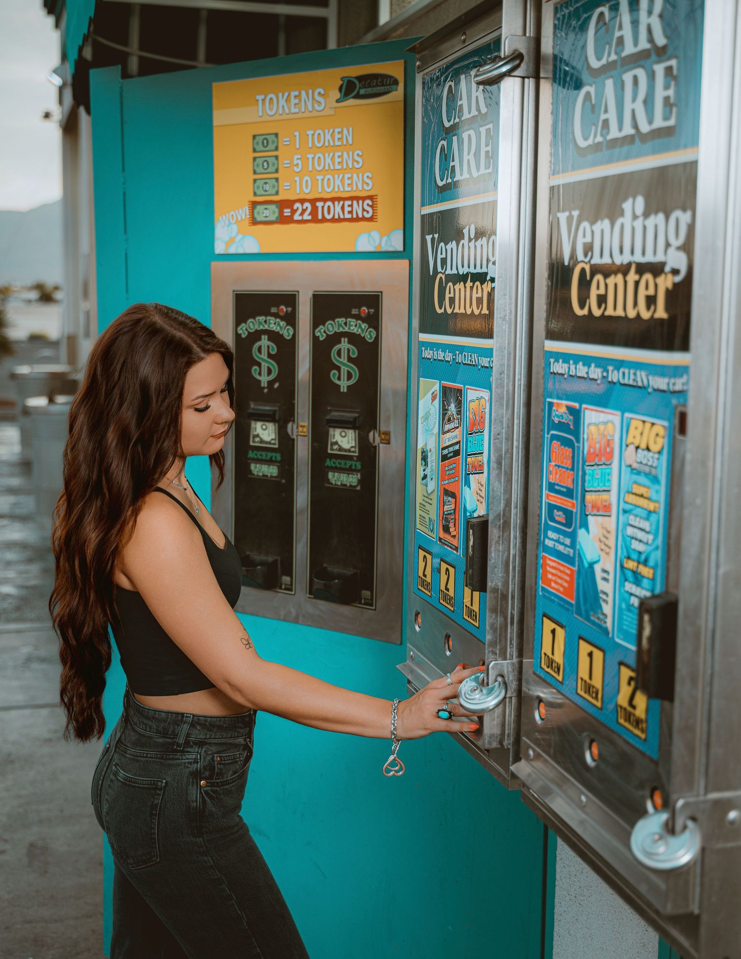 Young woman using a teal Car Care Vending Center token machine at a self-service car wash.