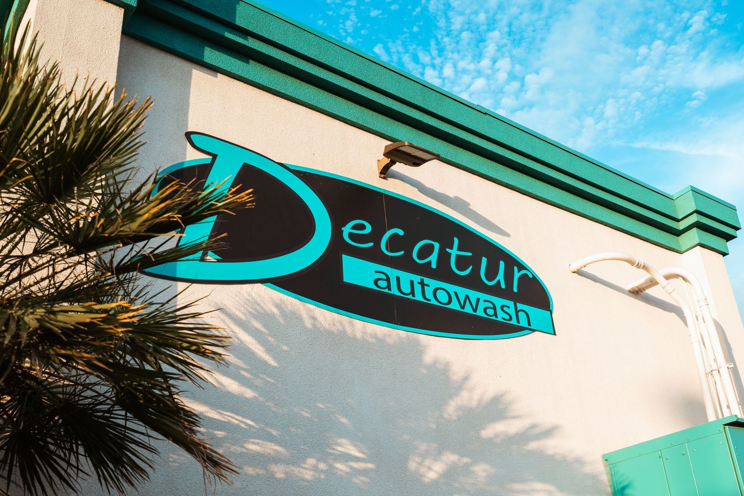 Decatur Autowash sign on a bright teal-trimmed building with palm trees under a blue sky.