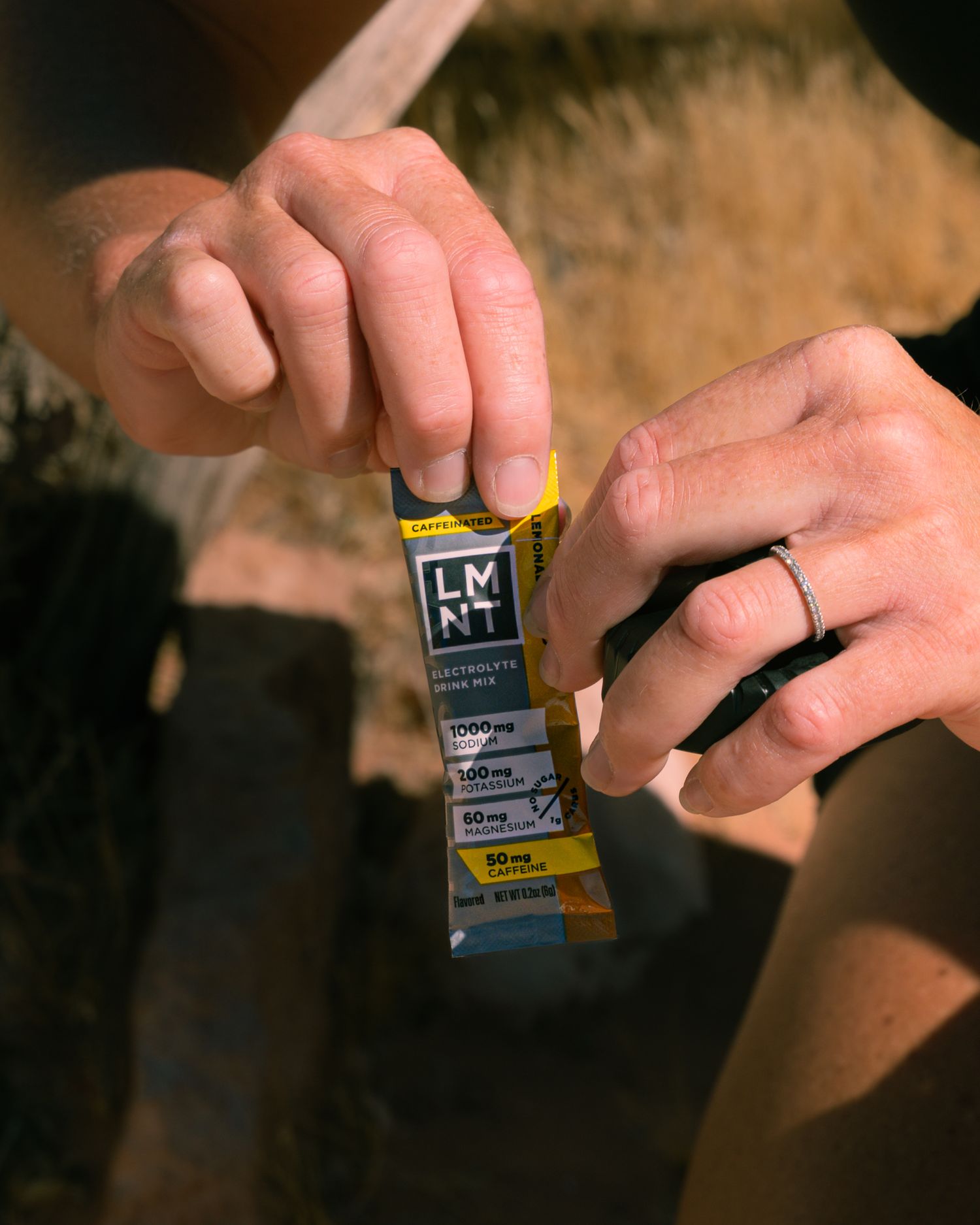 Hands tearing open an LMNT electrolyte powder packet showing sodium and potassium nutrition facts.