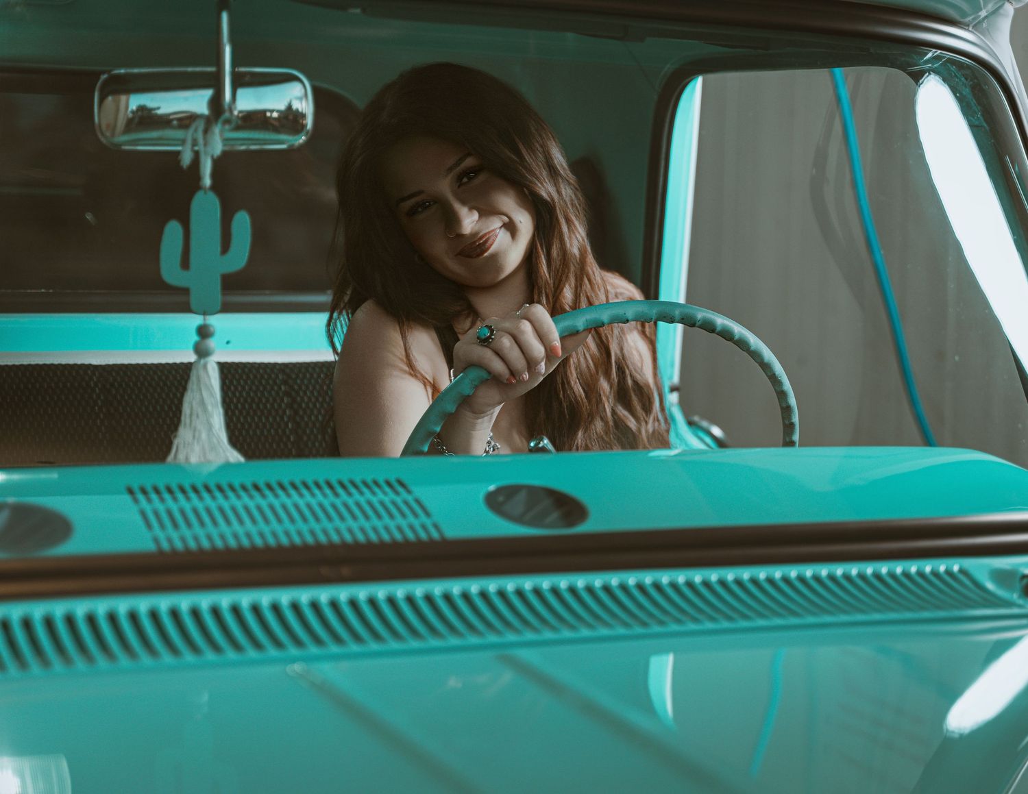 Young woman smiling behind turquoise vintage van steering wheel with cactus decoration.