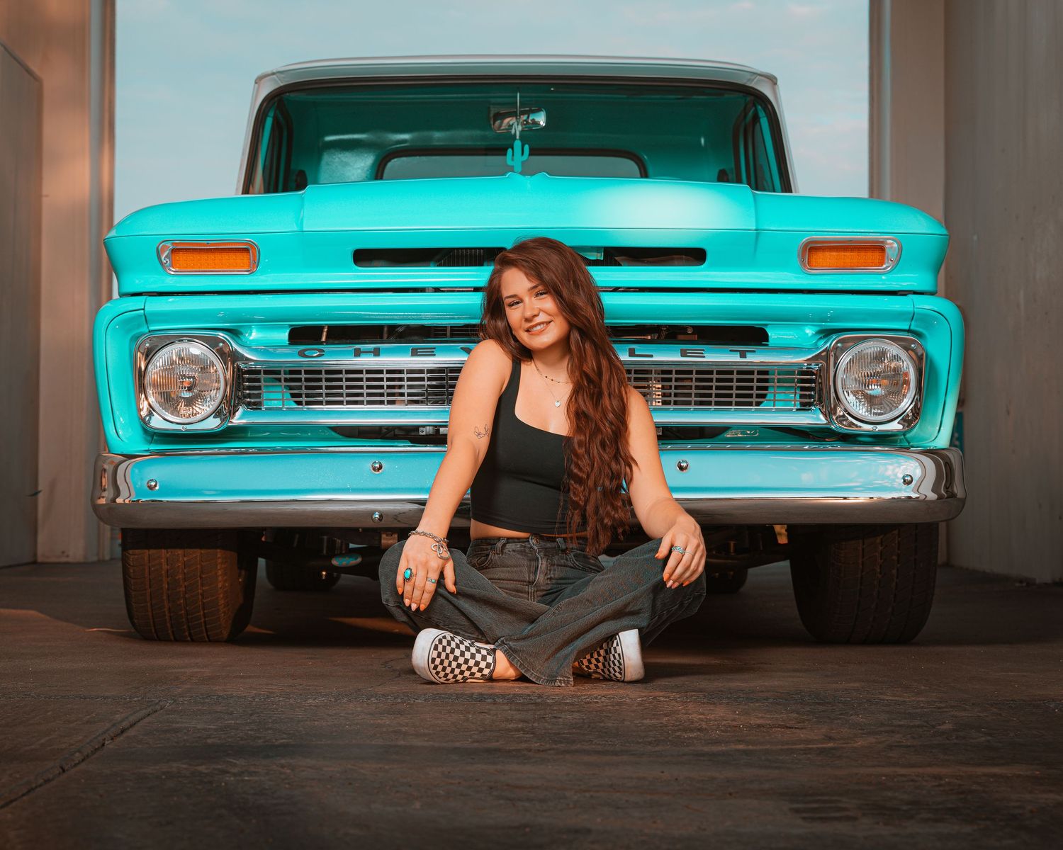 Young woman sitting in front of a classic turquoise pickup truck in a garage setting.