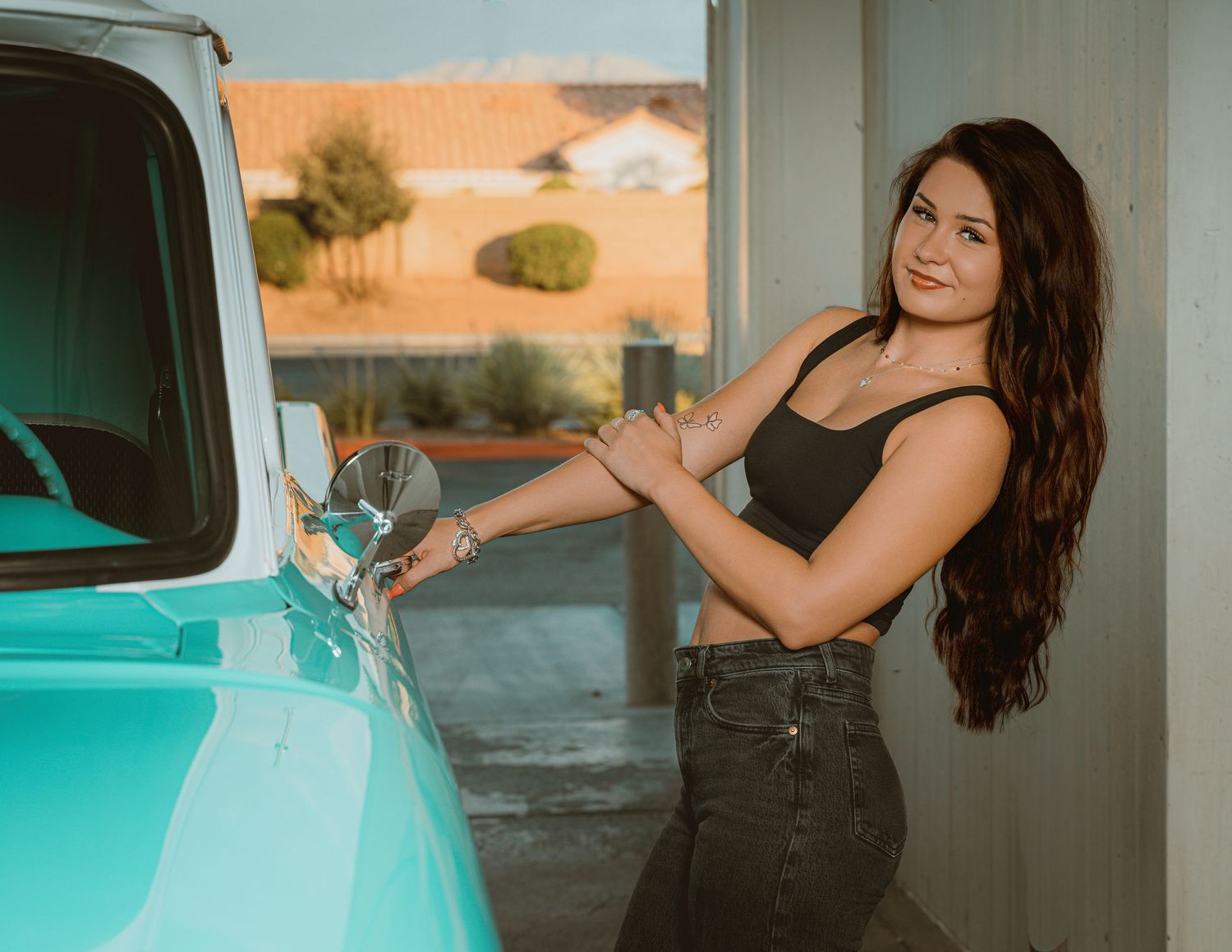 Young woman with long brown hair smiling while polishing a vintage turquoise truck outdoors.