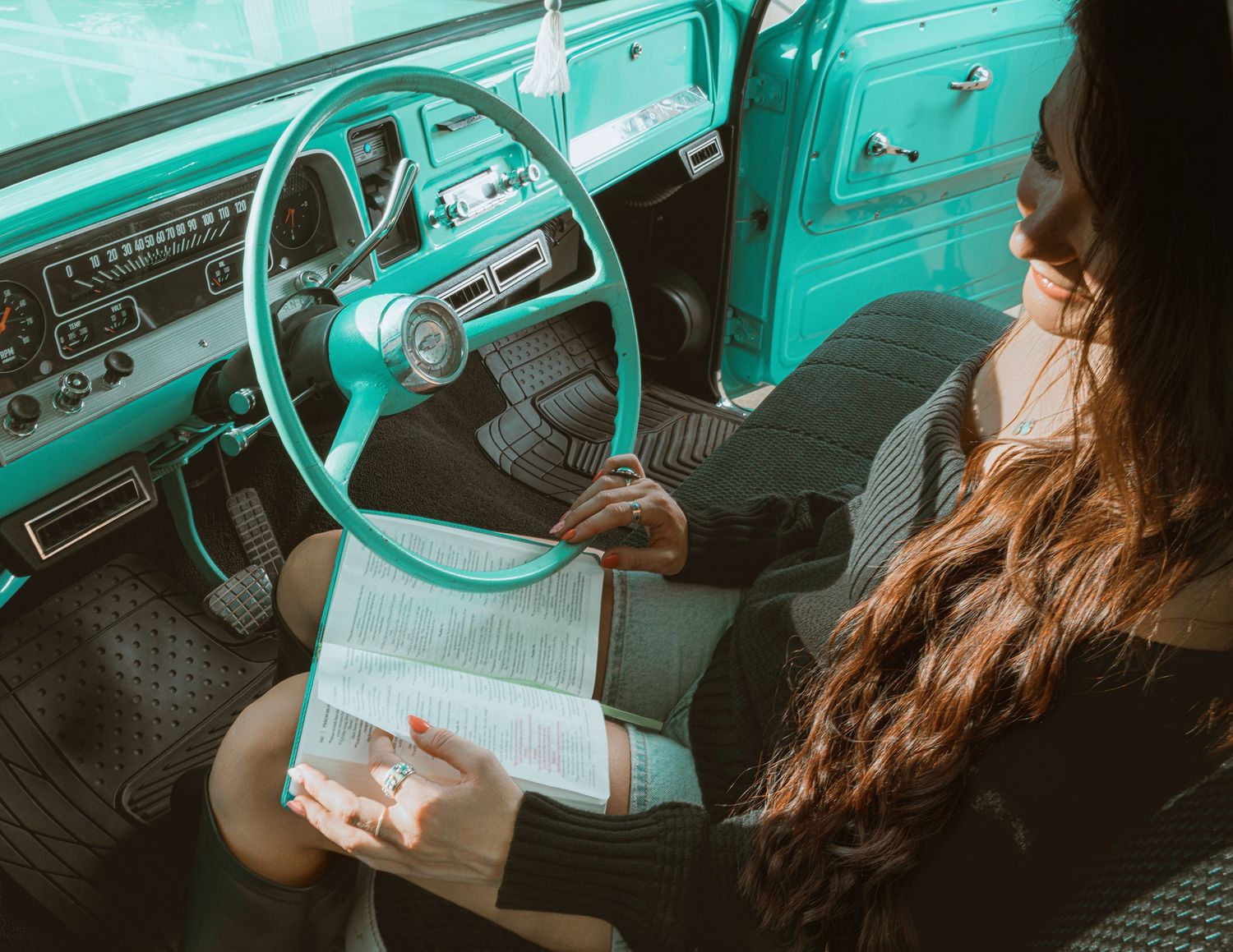 Woman reading a book inside a vintage teal truck with matching steering wheel.