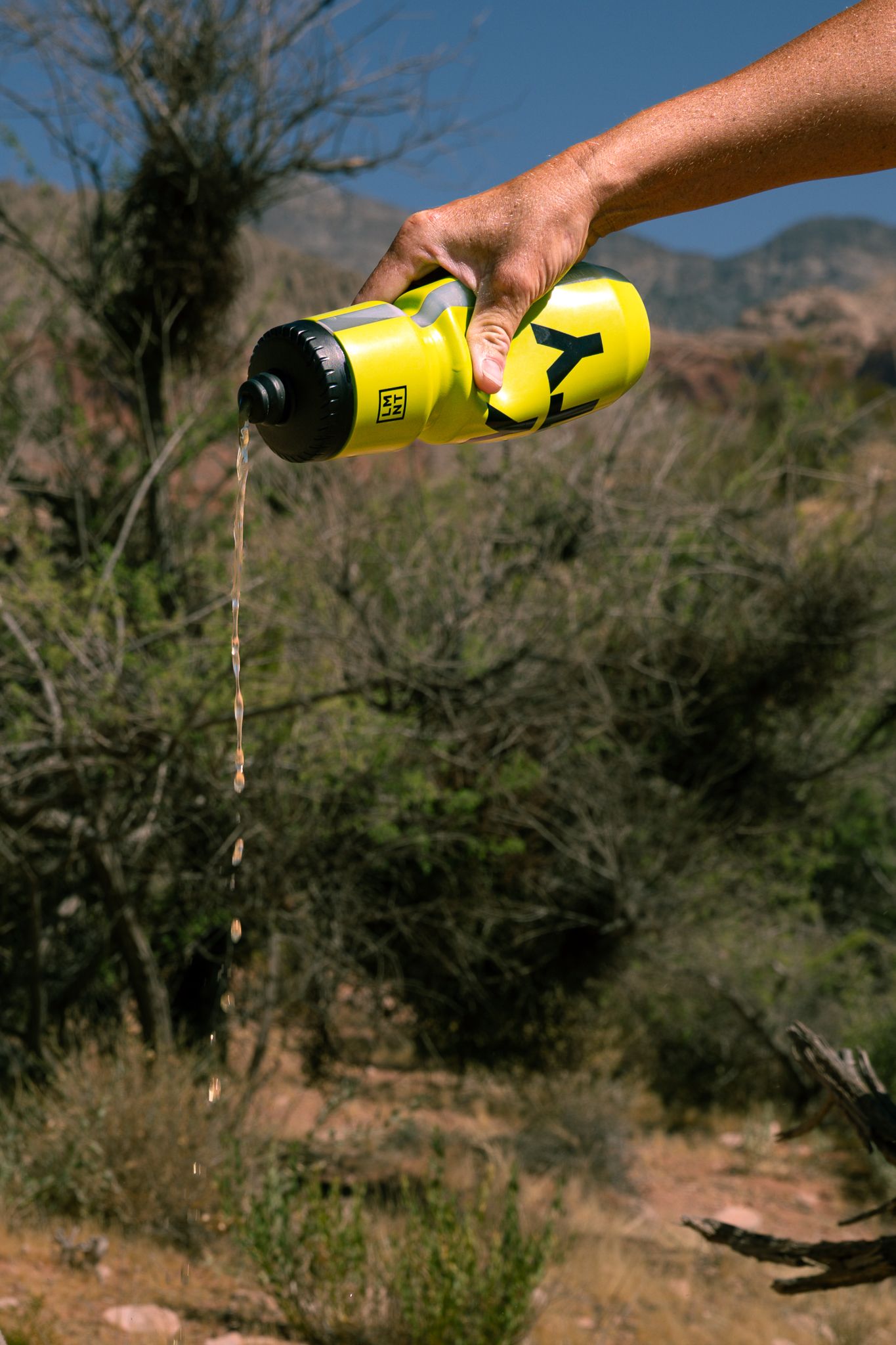 Hand pouring filtered water from yellow LMNT sports bottle in outdoor desert mountain setting.