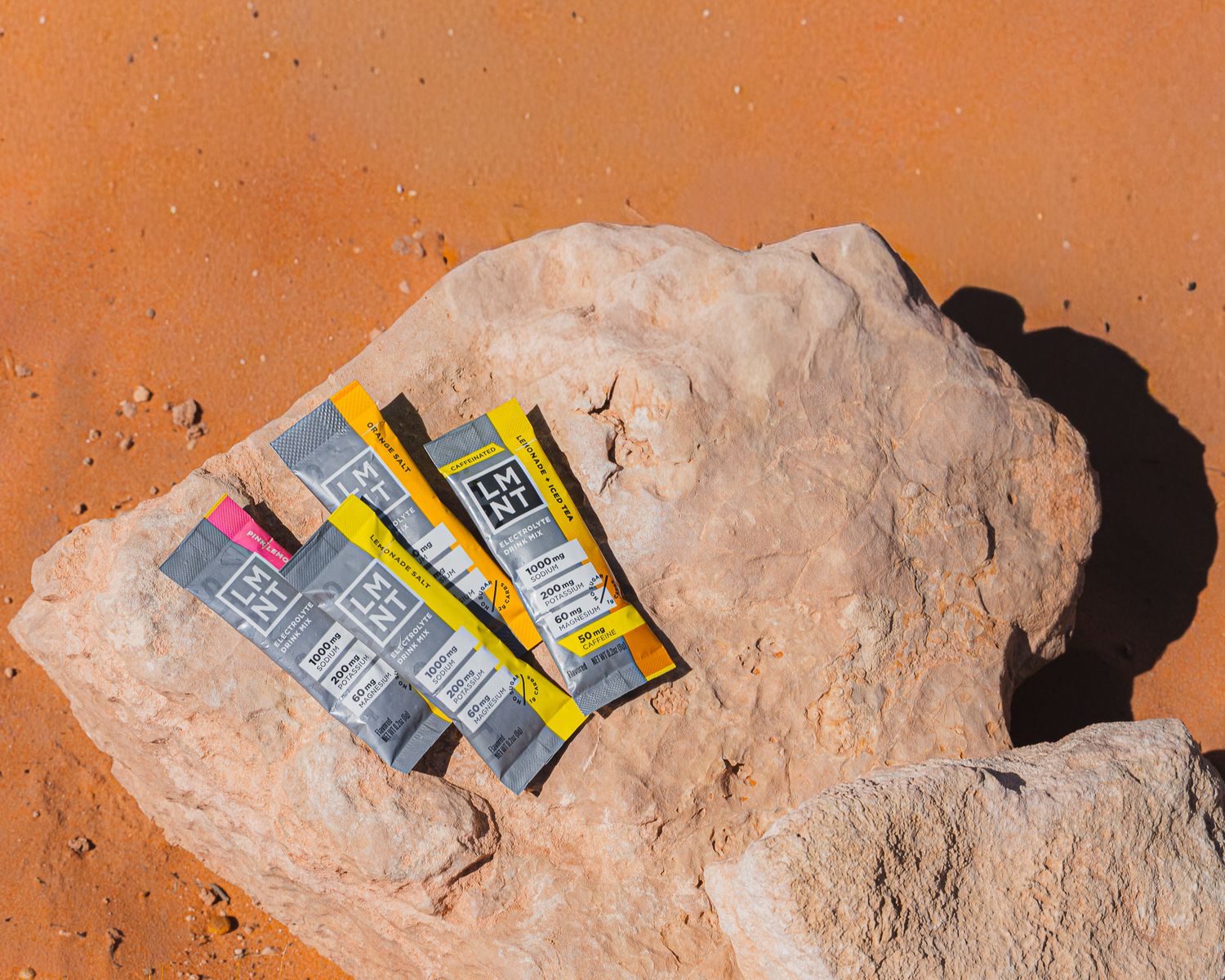 LMNT electrolyte drink mix packets resting on a desert boulder surrounded by red sand terrain.