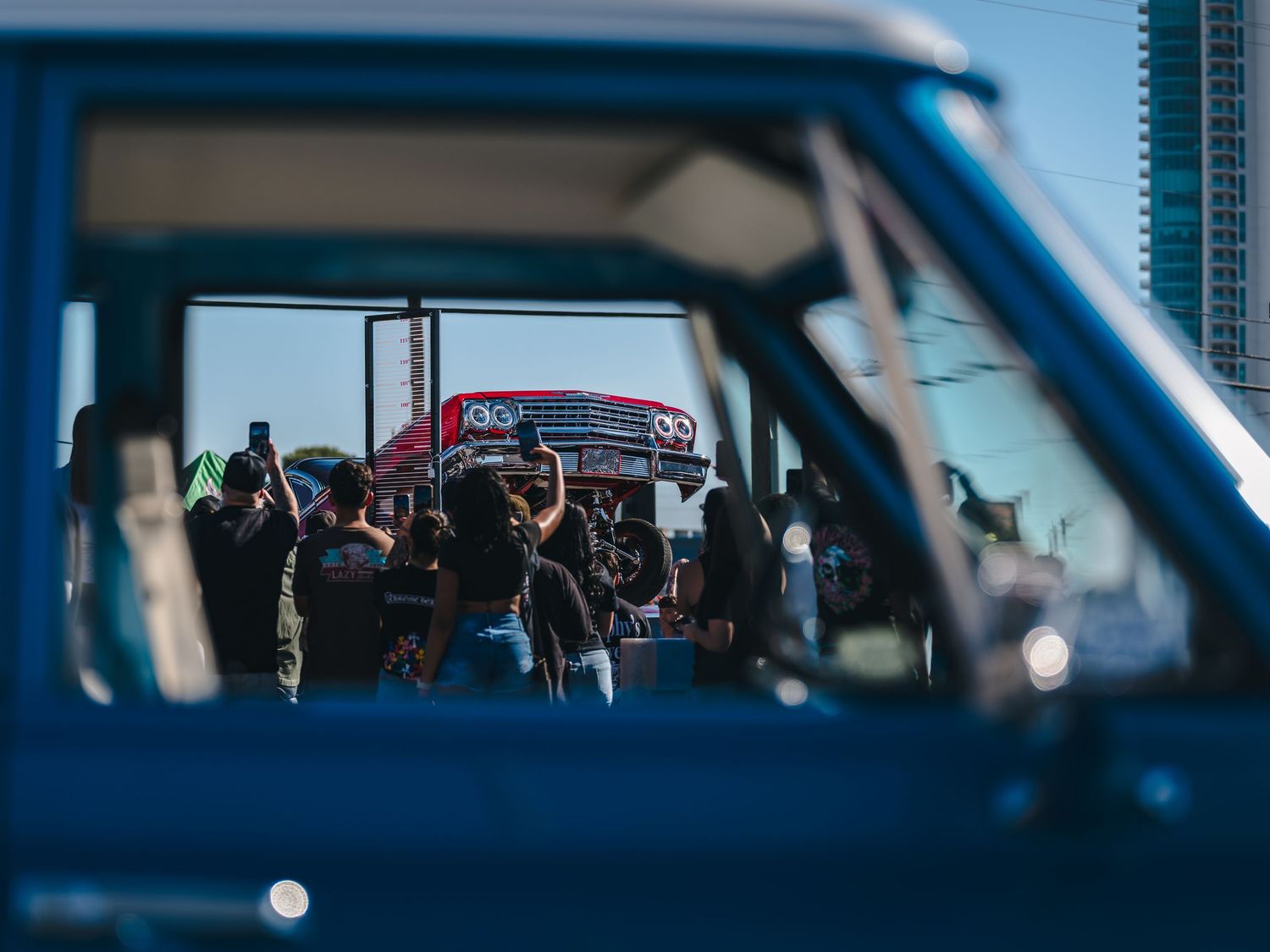 Crowd of people photographed through a vintage blue truck window at an outdoor car show event.
