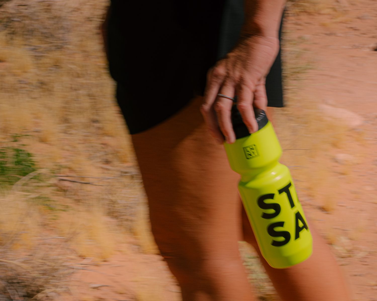 Close-up of a hand holding a bright yellow STAY SALTY LMNT electrolyte drink bottle during a trail run.