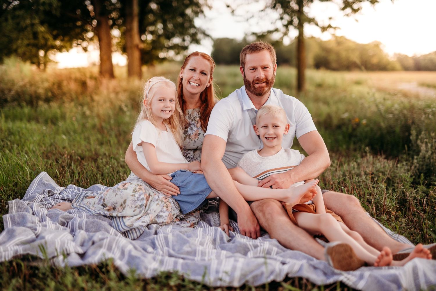 A family sits together on a blanket in a sunlit meadow during golden hour.