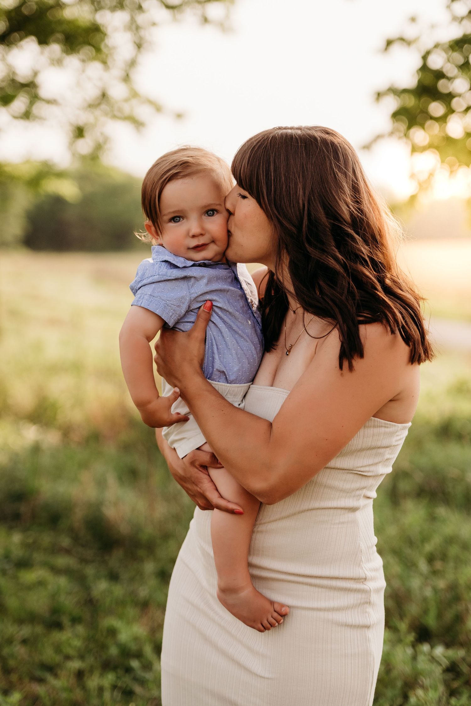 A tender moment captured between mother and baby at sunset in a grassy field, lit by golden hour sunlight at Prophetstown State Park