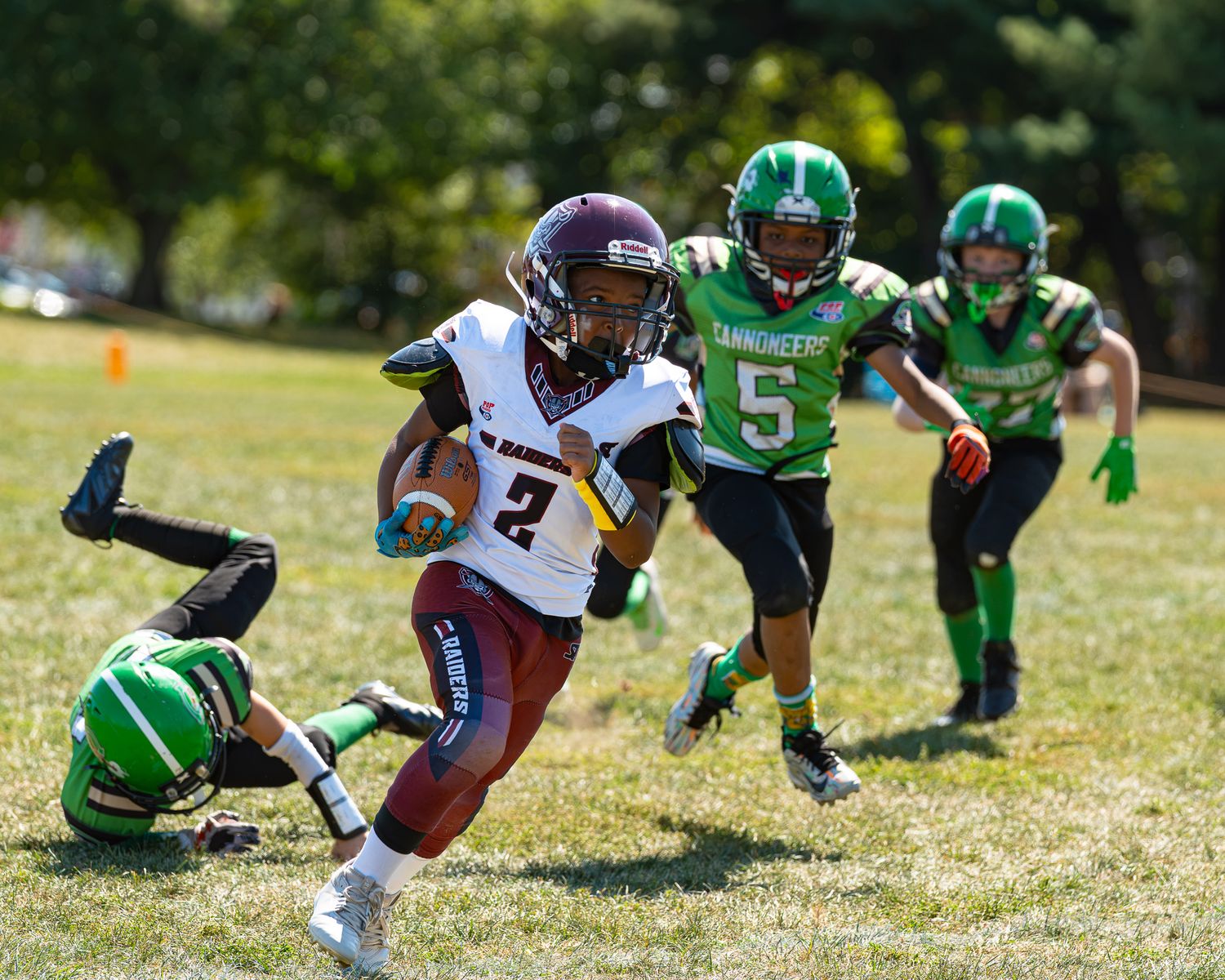 abington raiders football player running with the ball tucked in the right arm being chased by three opposing players