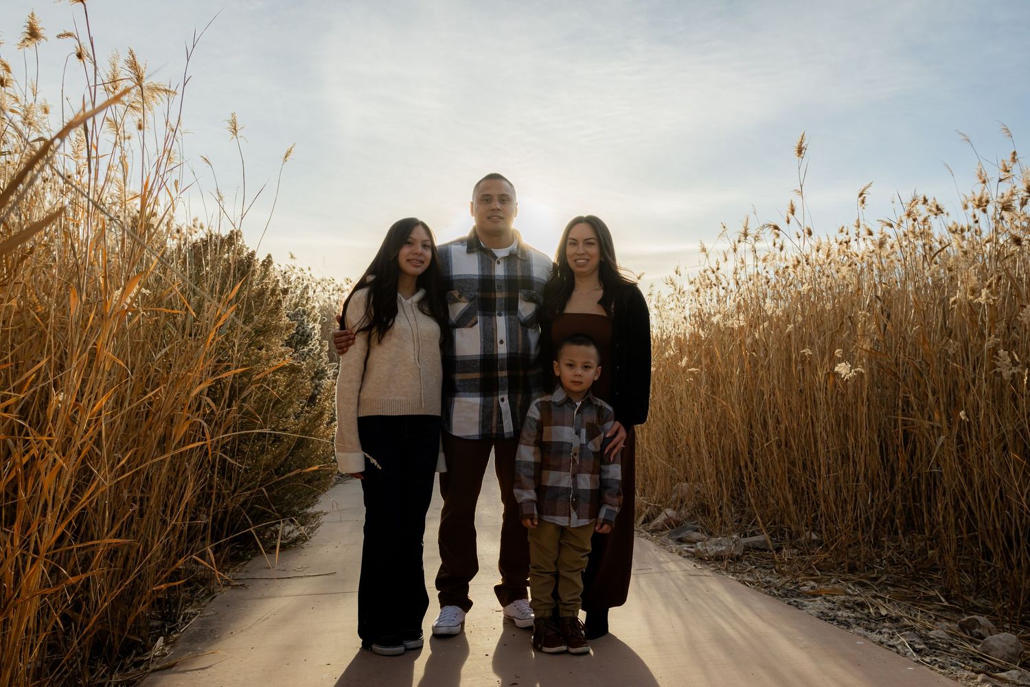 Family of four posing on a sunlit path surrounded by golden tall grass during a fall outdoor photo session.