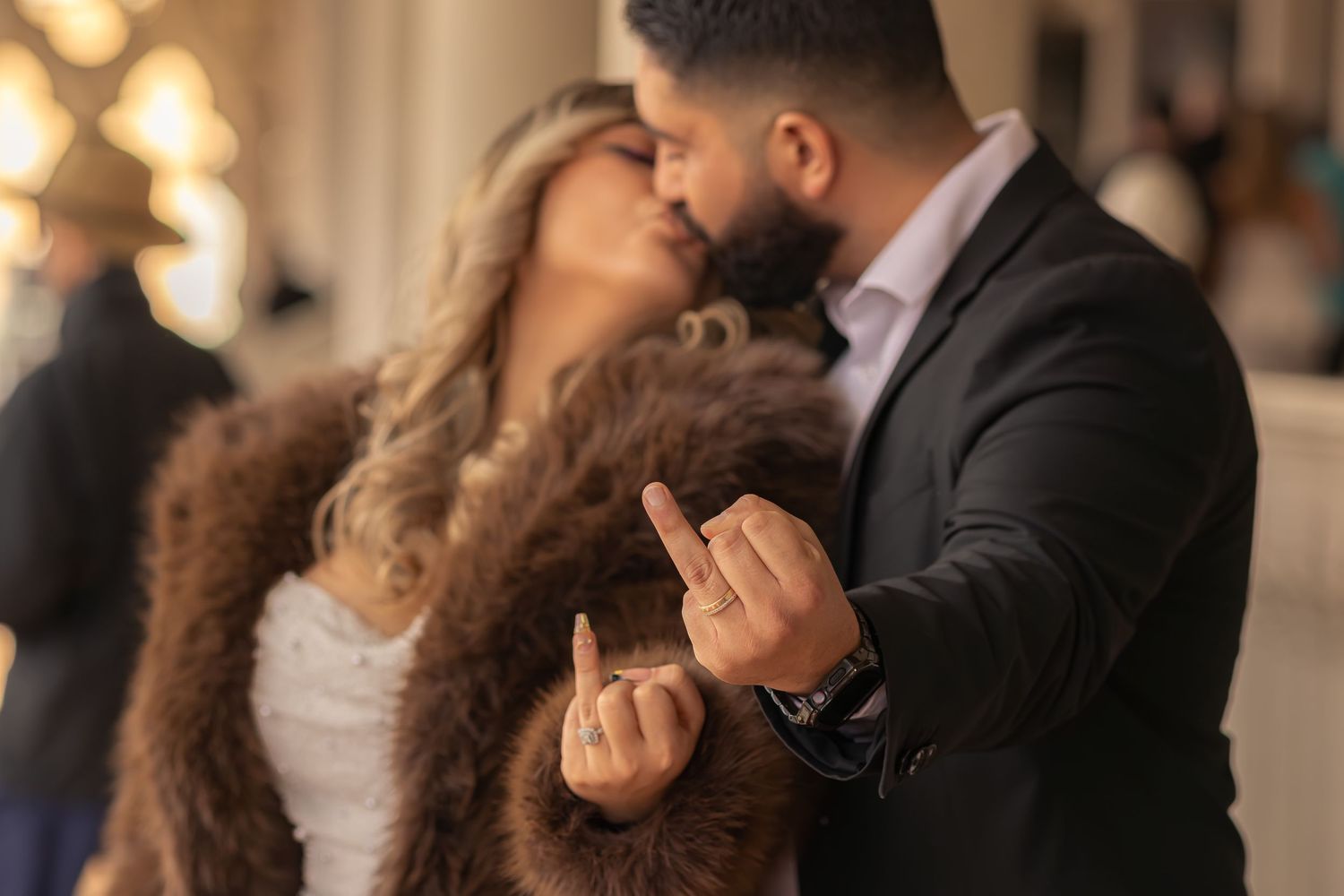 Couple sharing a romantic kiss while showing off engagement ring at elegant venue.