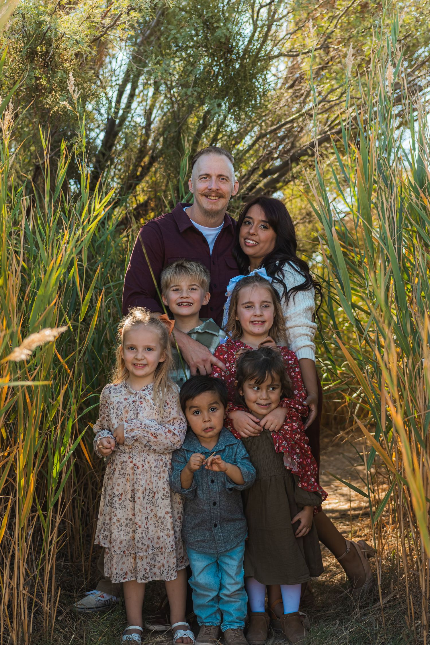 Family of seven posing among tall green reeds in a natural outdoor setting.