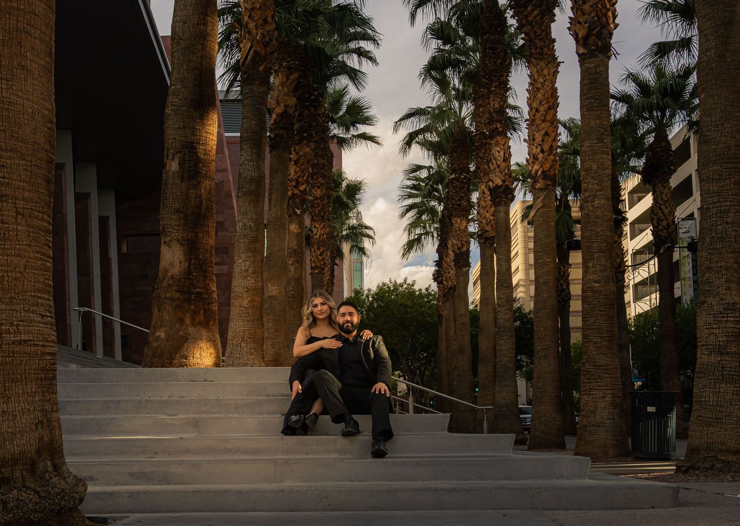 Couple sitting together on steps surrounded by tall palm trees at dusk in Las Vegas.