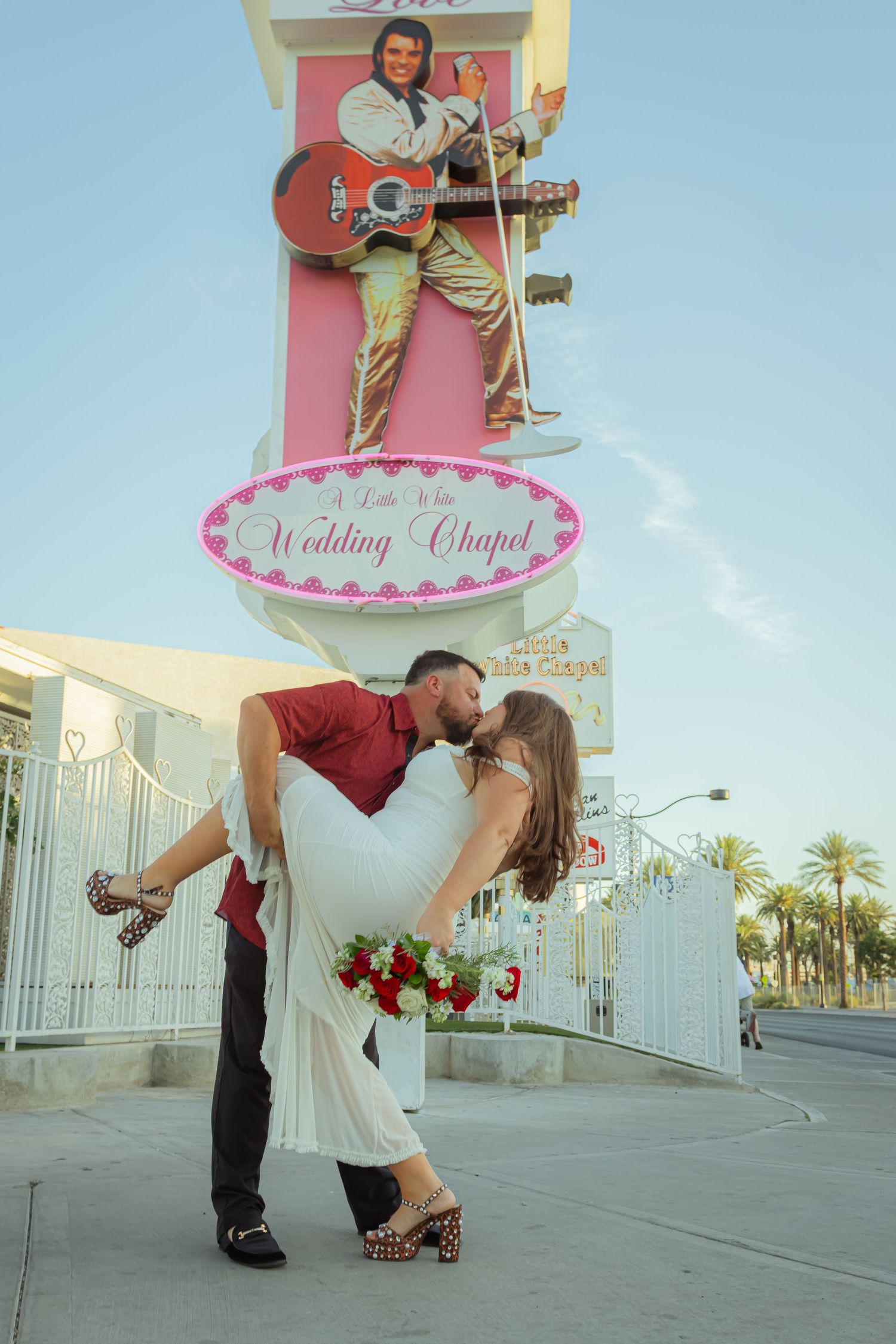 Newlyweds sharing a kiss outside A Little White Wedding Chapel with Elvis sign in Las Vegas.