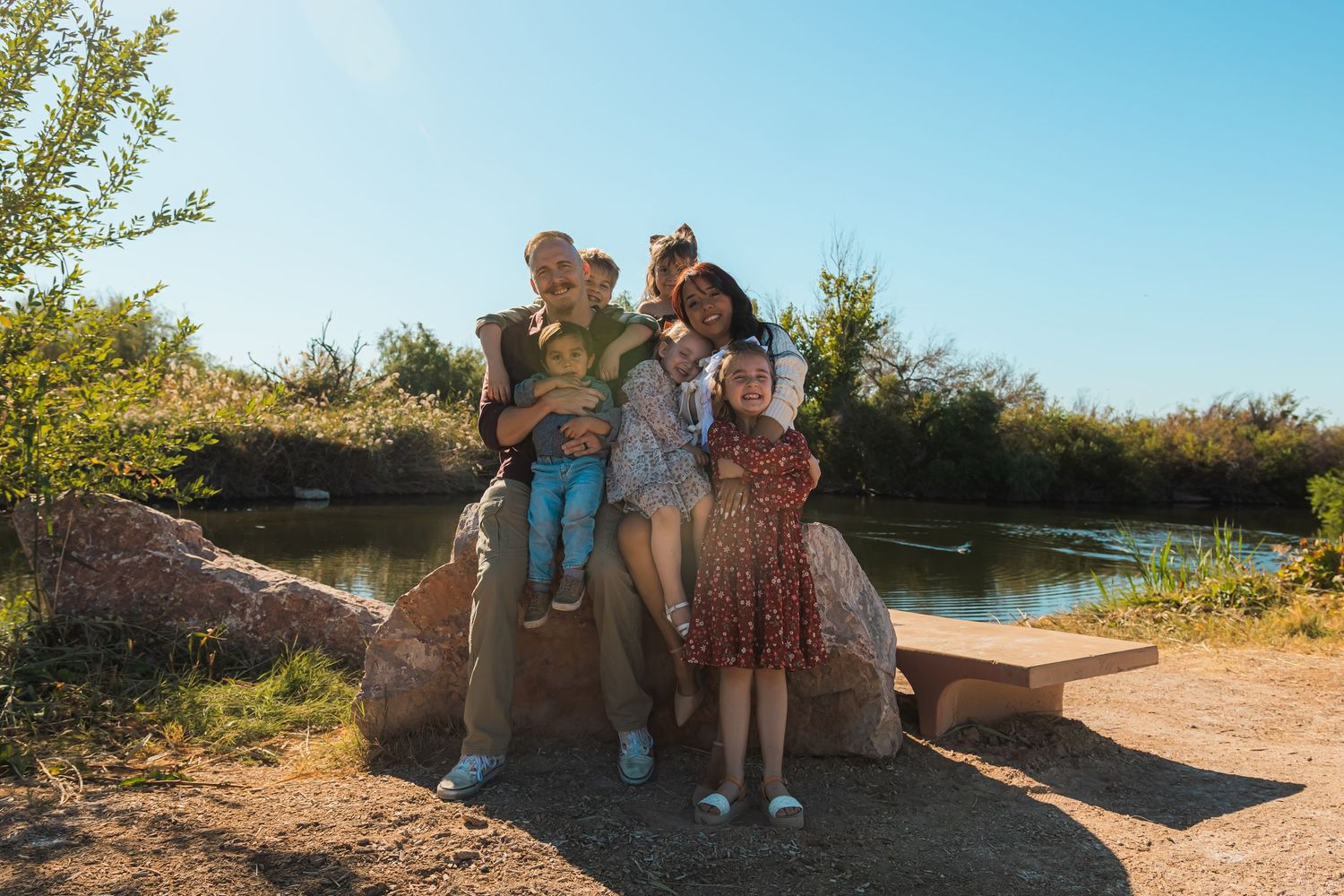 Family posing on large rocks near a peaceful pond on a sunny day.