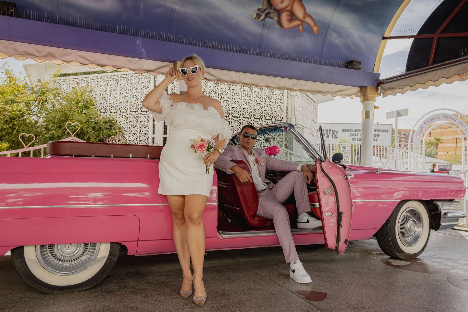 Bride in white mini dress and groom beside a vintage pink Cadillac convertible at Las Vegas chapel.
