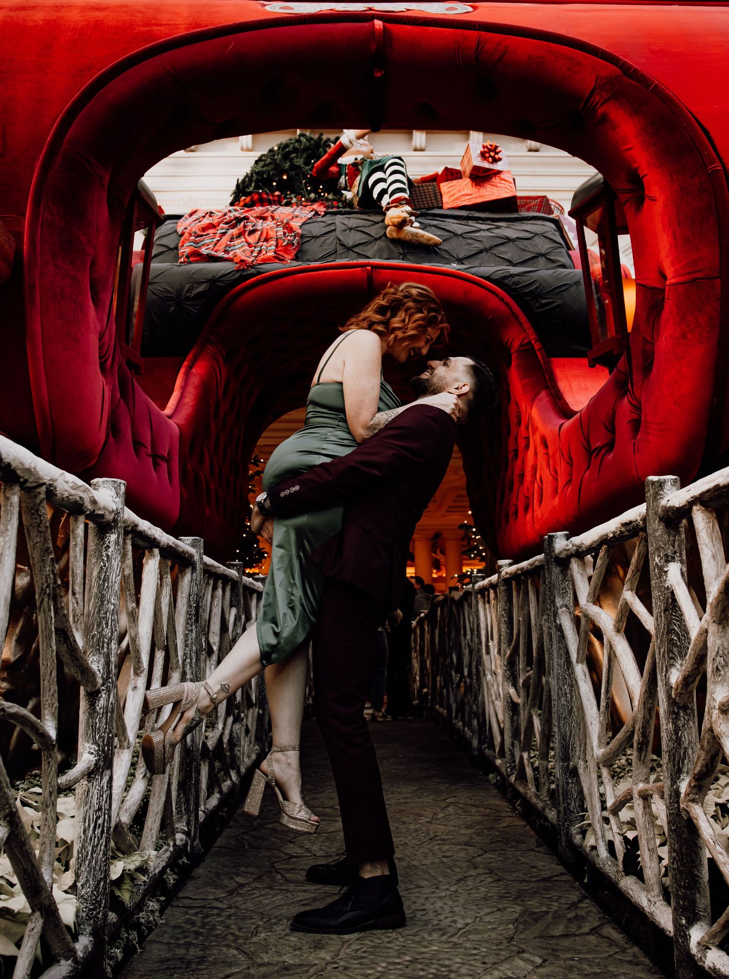 Couple sharing passionate kiss in red vintage car trunk decorated for Christmas on rustic bridge.