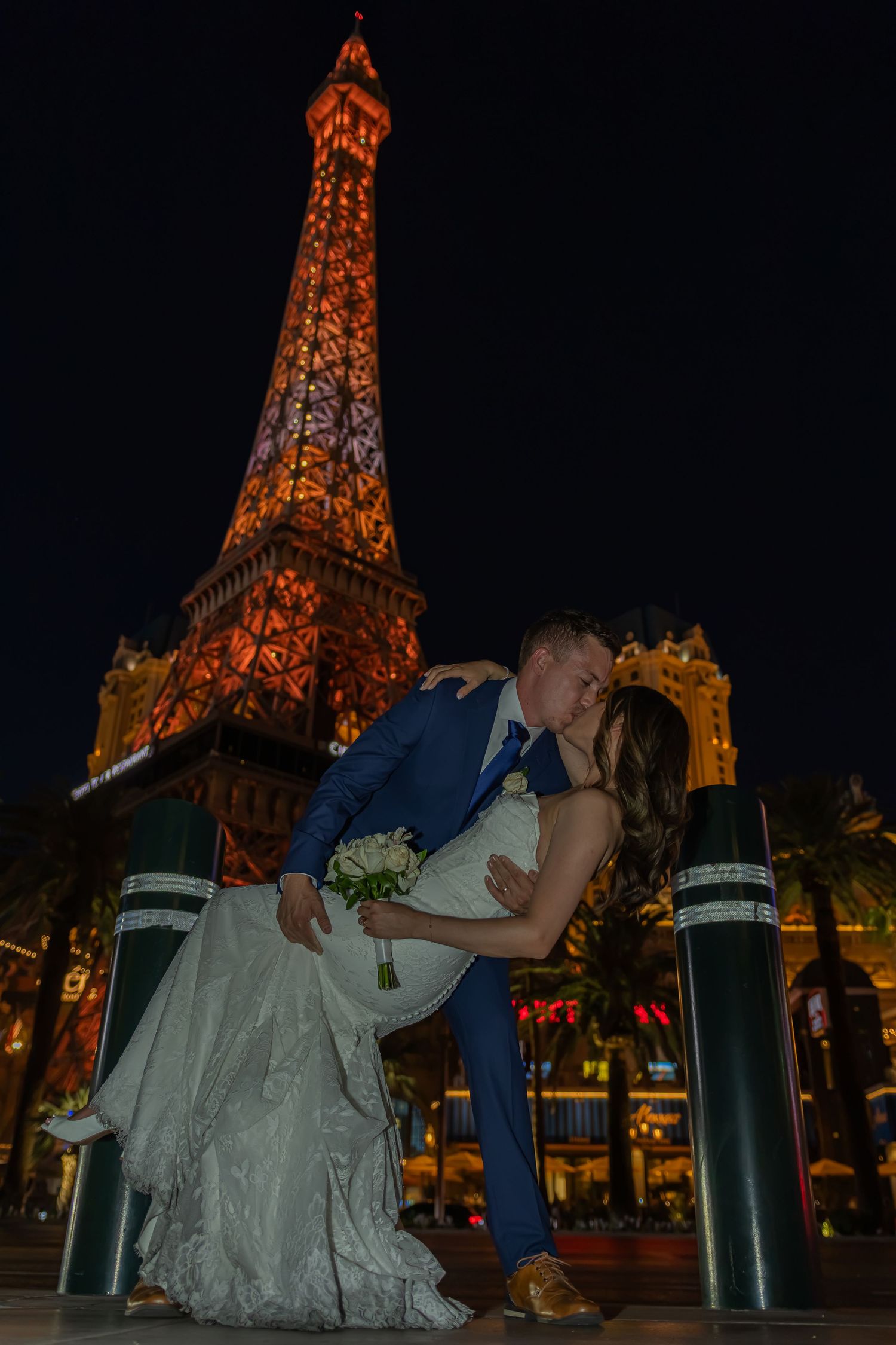 Bride and groom share a romantic dip kiss in front of the illuminated Eiffel Tower in Las Vegas.