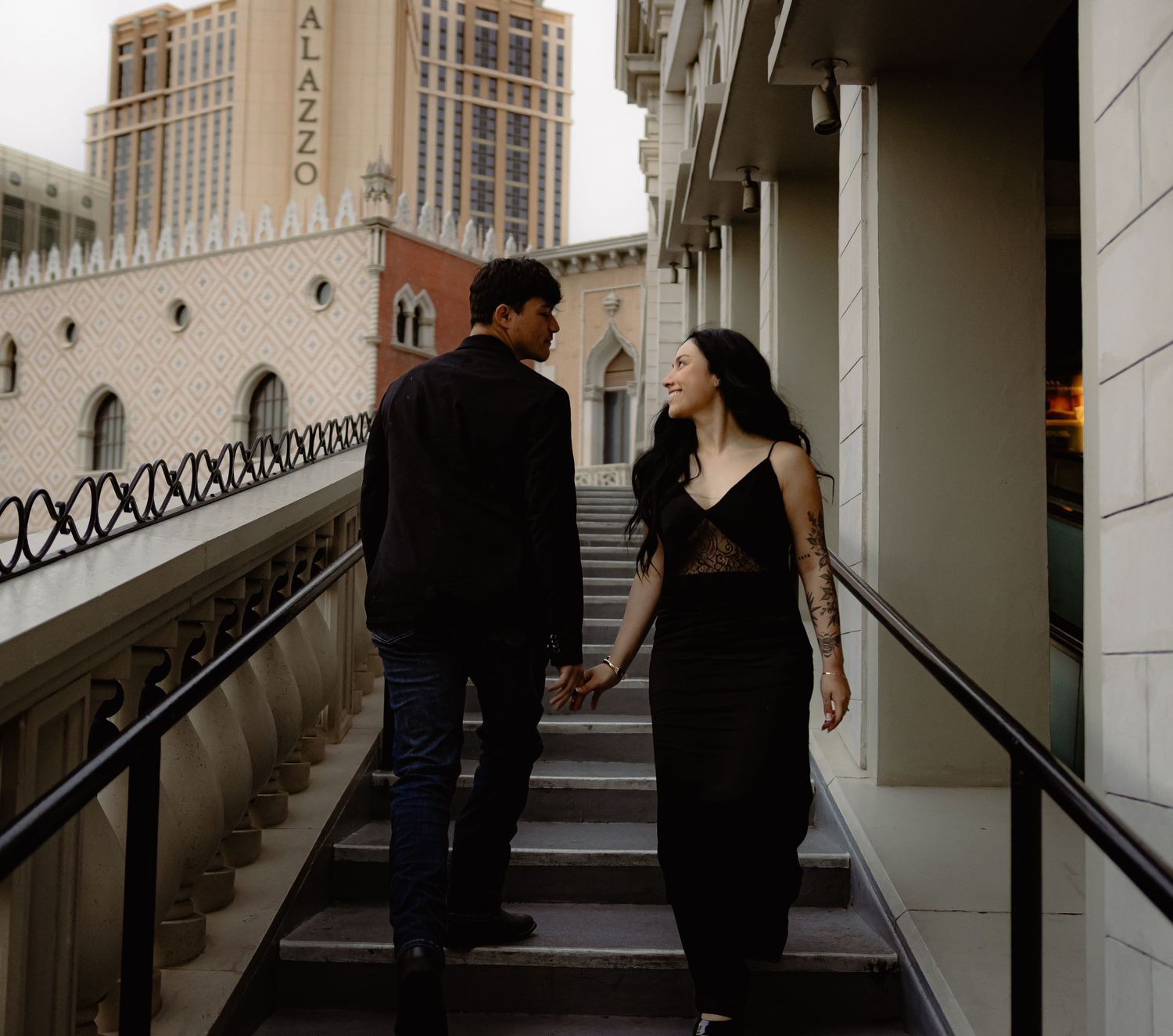 Couple holds hands walking up stairs near the Palazzo hotel in Las Vegas at dusk.