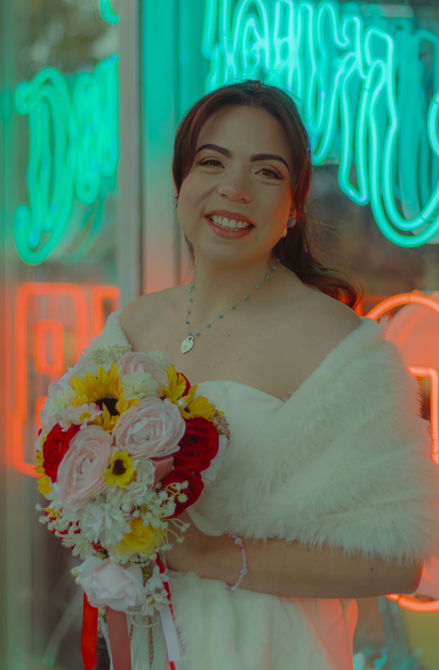 Radiant bride smiles holding a colorful bouquet of roses and sunflowers in front of neon signs.