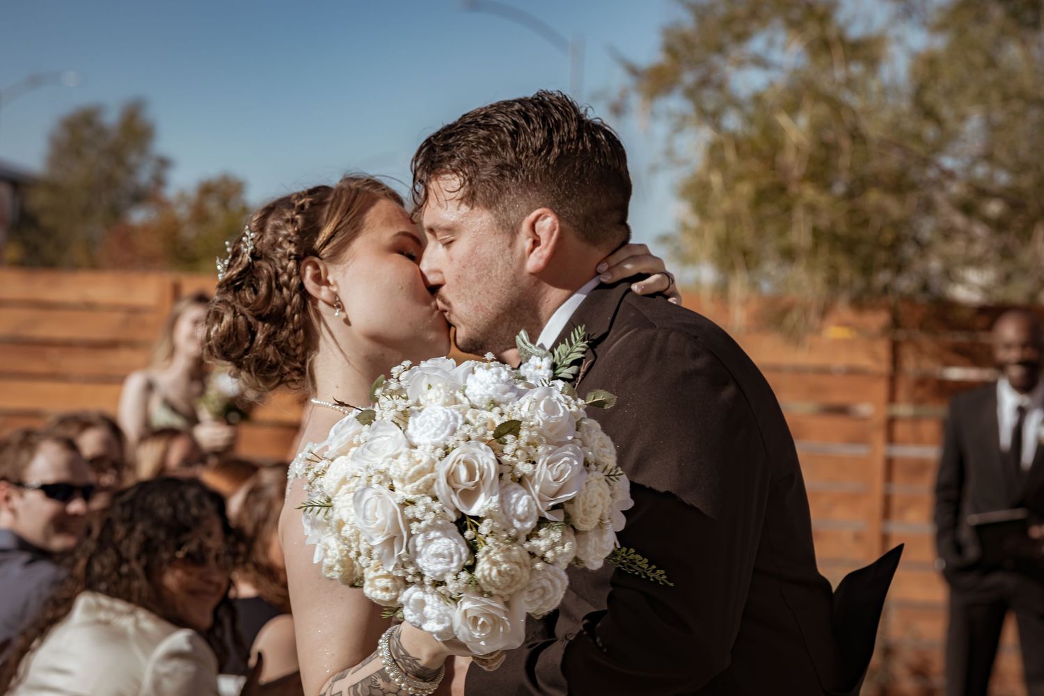 Bride and groom share first kiss at altar, bride holding large white rose bouquet.