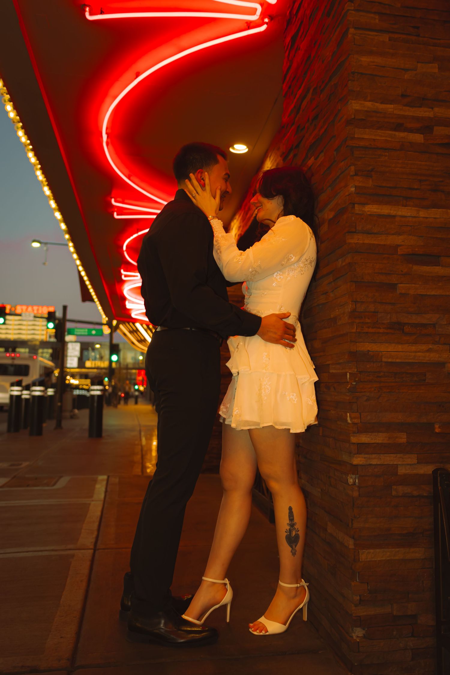 Couple kissing against a brick wall beneath glowing red neon signs at dusk on Fremont Street Las Vegas.
