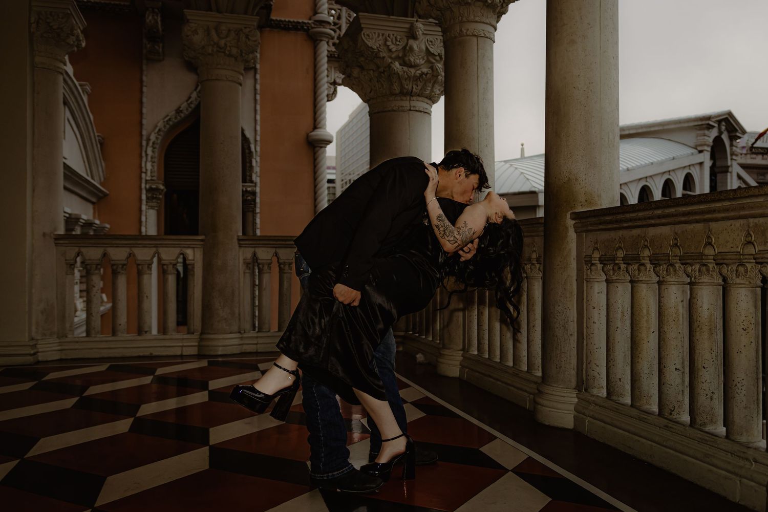 Couple sharing a dramatic dip kiss in an elegant columned arcade with checkered floors at The Venetian.