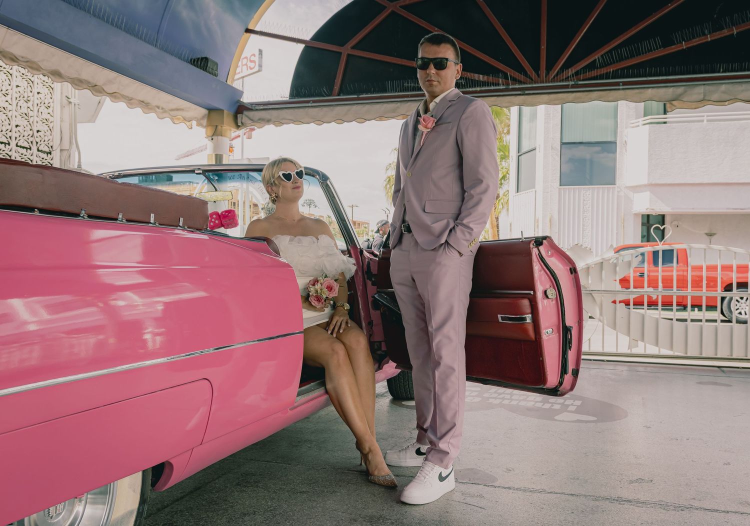 Bride and groom posing with a classic pink convertible car at a Las Vegas wedding venue.