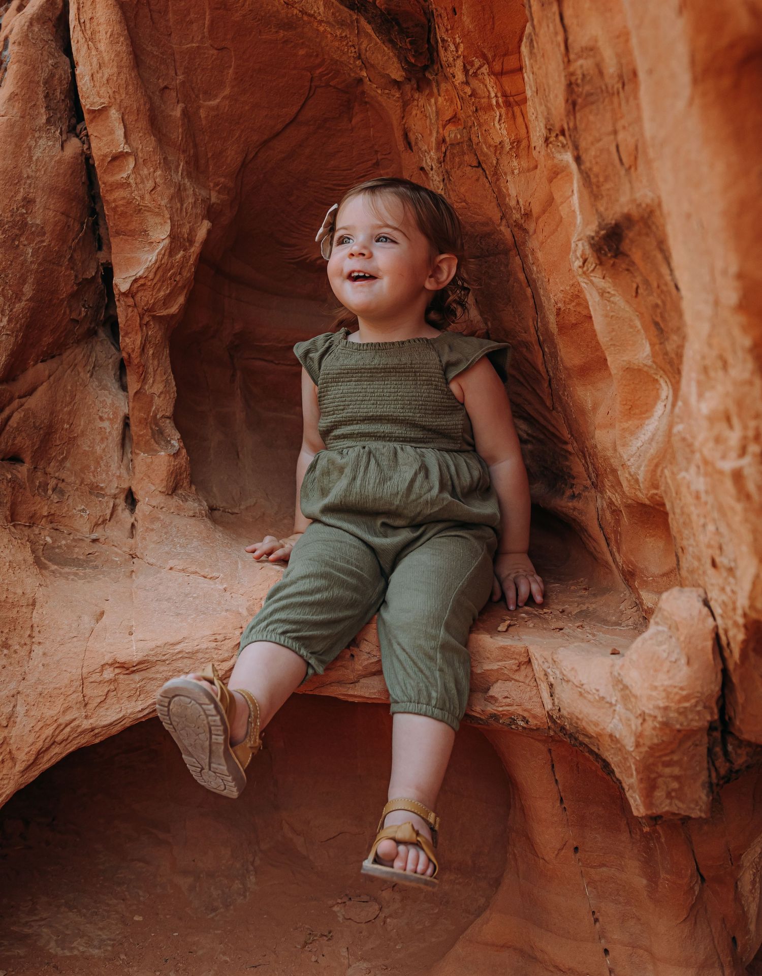 Happy toddler in green outfit sitting in a carved red sandstone rock niche outdoors.