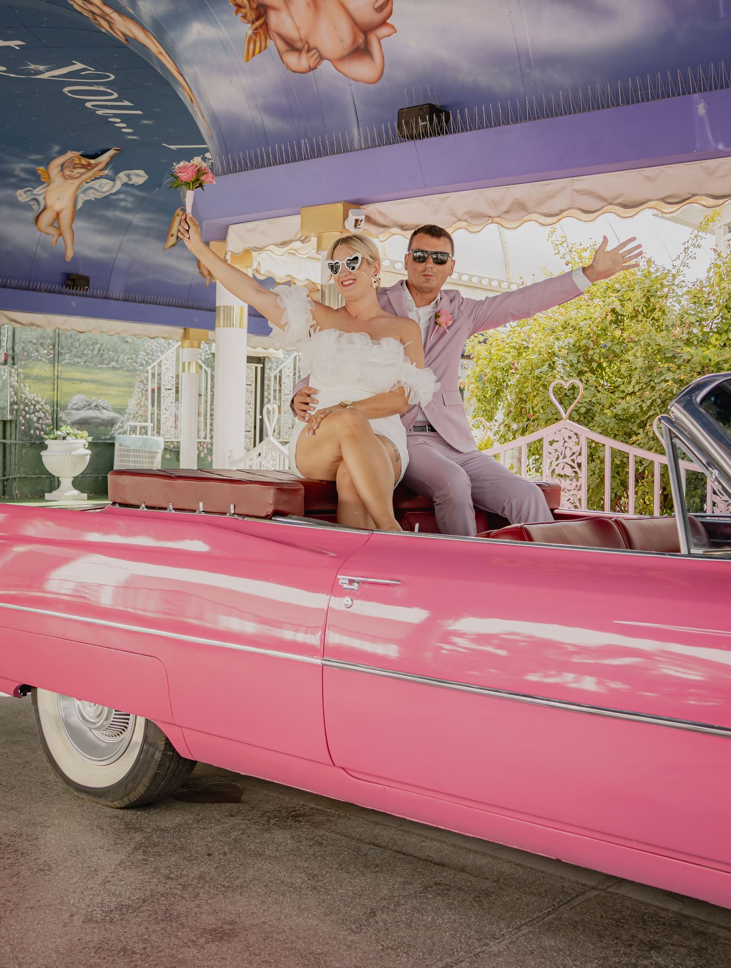 Joyful newlyweds celebrating in a classic pink convertible at a Las Vegas wedding chapel.