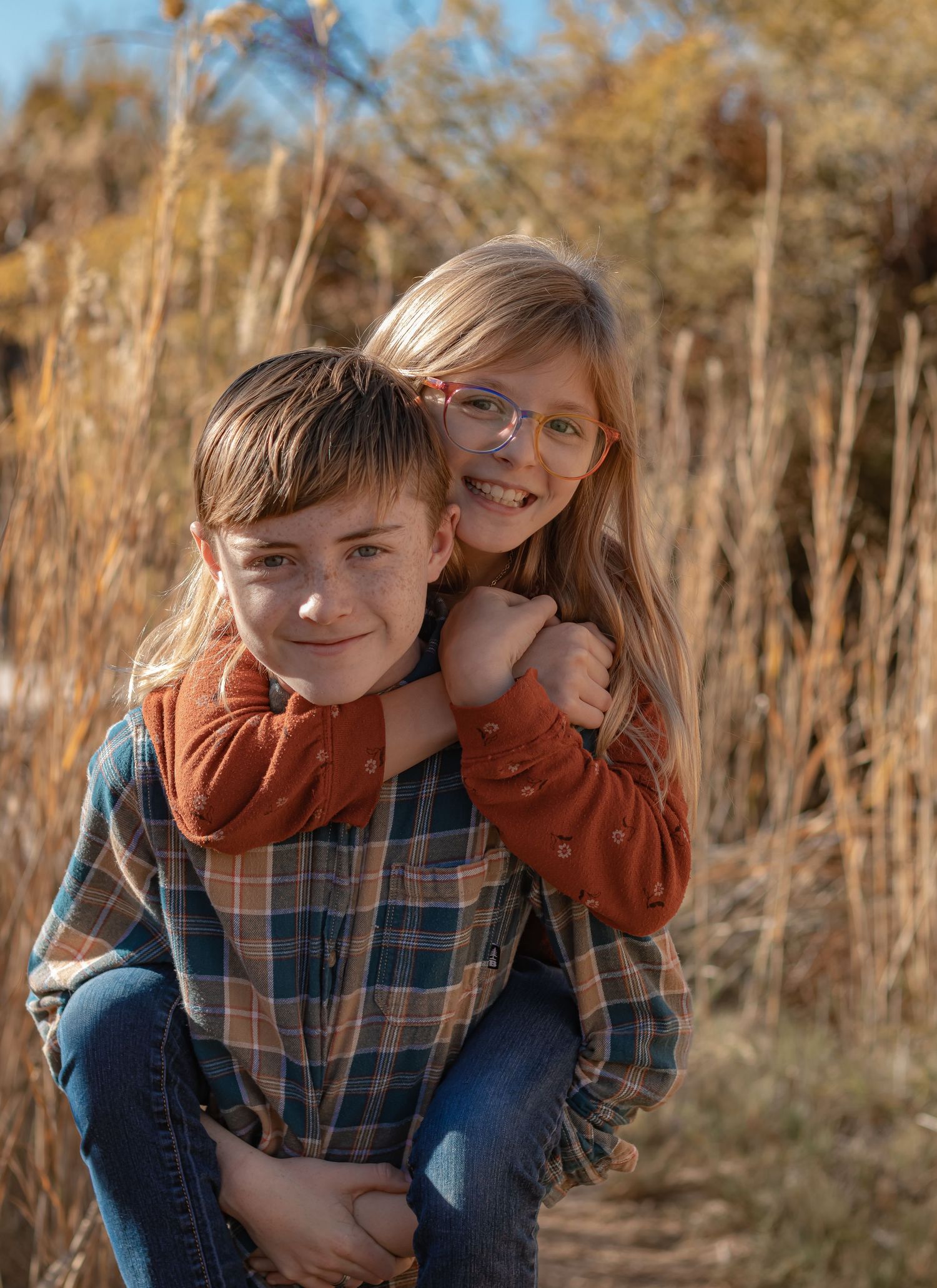 A boy gives a smiling girl a piggyback ride in a warm golden outdoor setting.