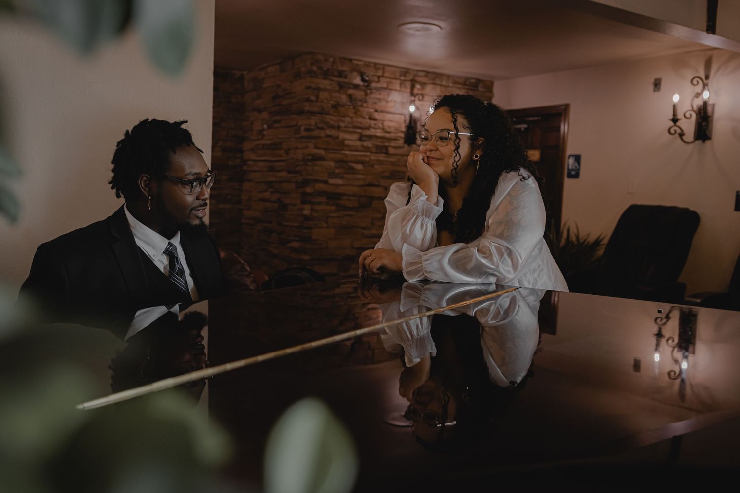 Couple shares an intimate conversation at a dimly lit bar with stone wall background.