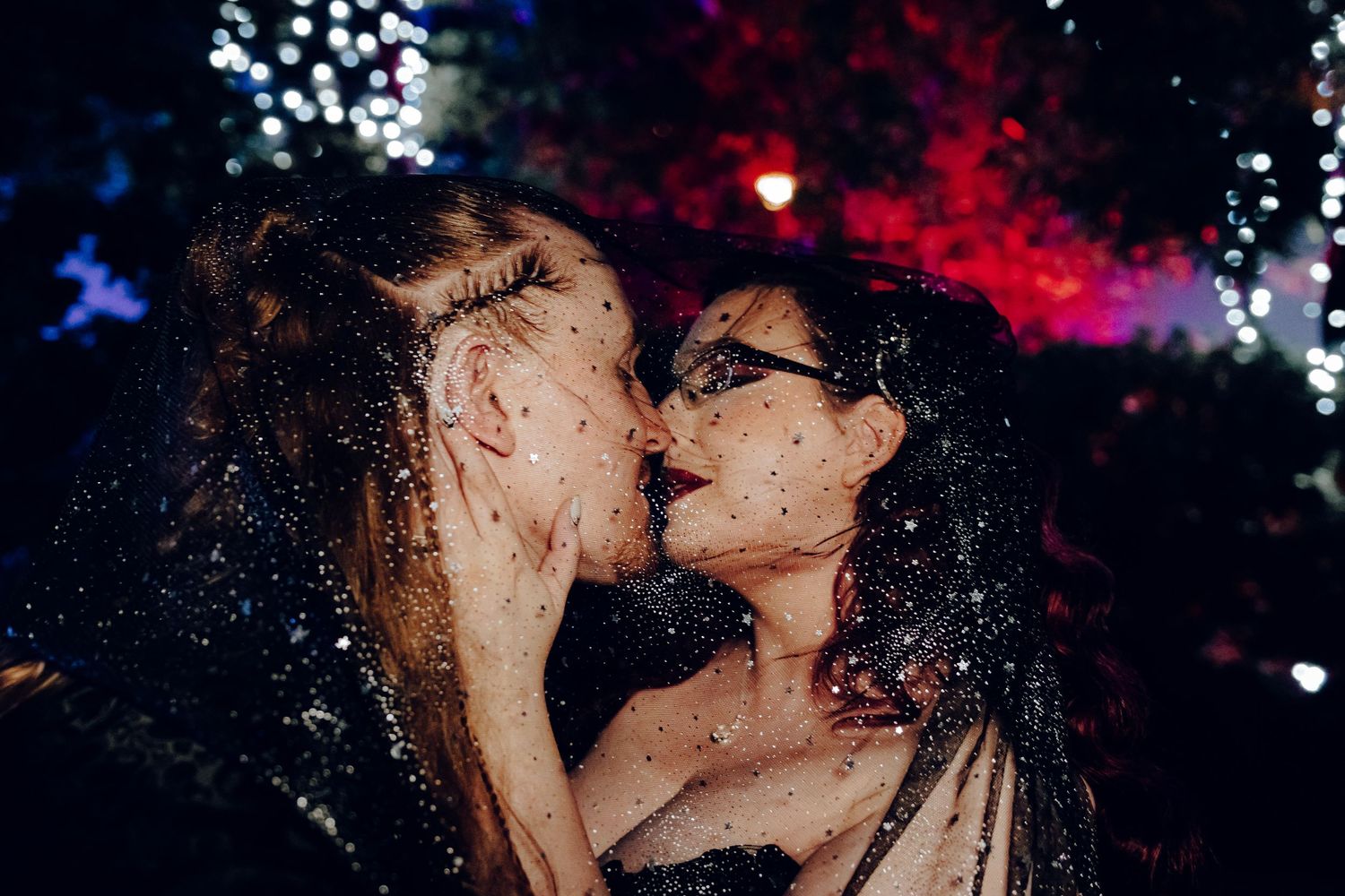 Gothic bride and groom share passionate kiss surrounded by sparkling glitter at night wedding.