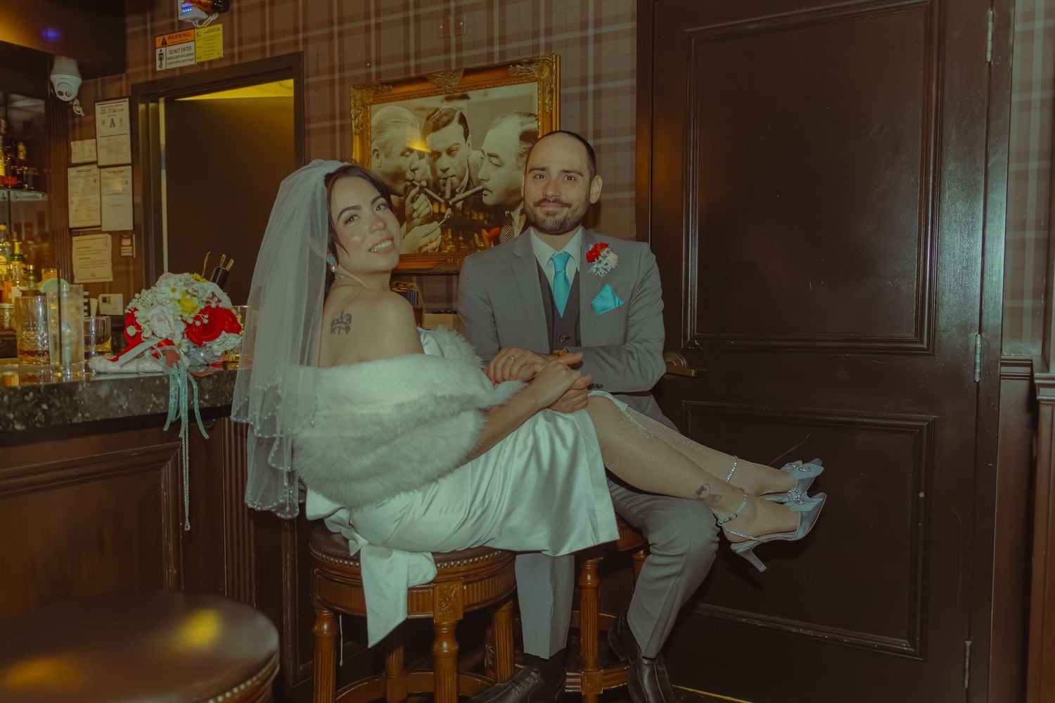 Bride and groom sit together intimately in a warmly lit vintage-style wedding venue interior.