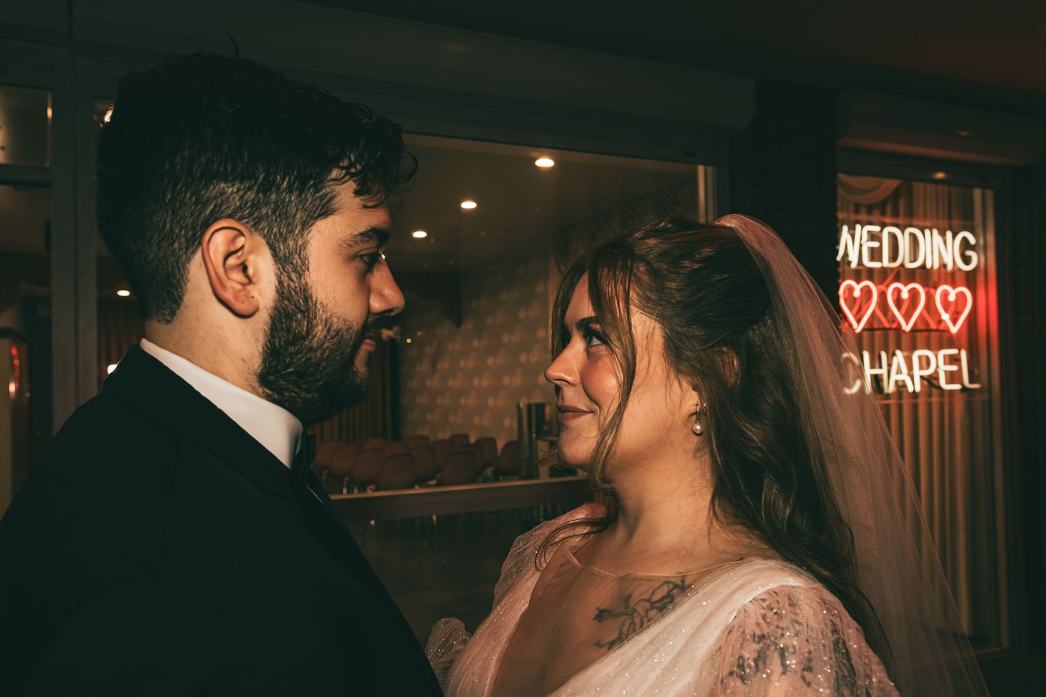 Bride and groom share an intimate moment in front of a glowing Wedding Chapel neon sign.