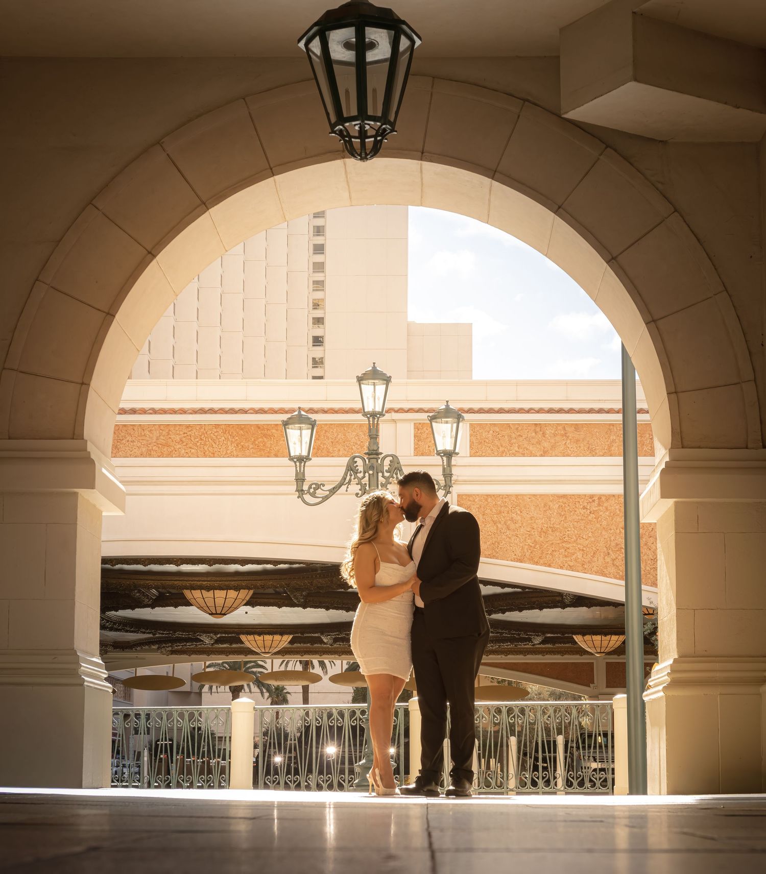 Couple kissing in golden sunlight beneath grand arch at The Venetian Las Vegas resort exterior.