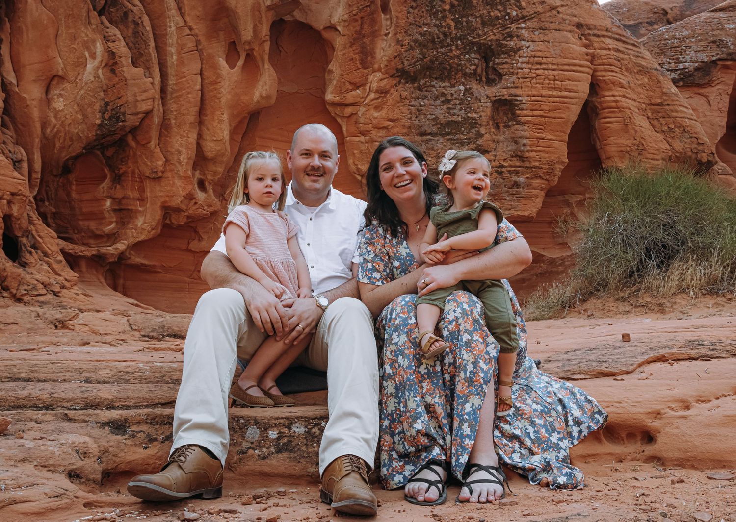 Family of four smiling together among red rock formations in a desert landscape.