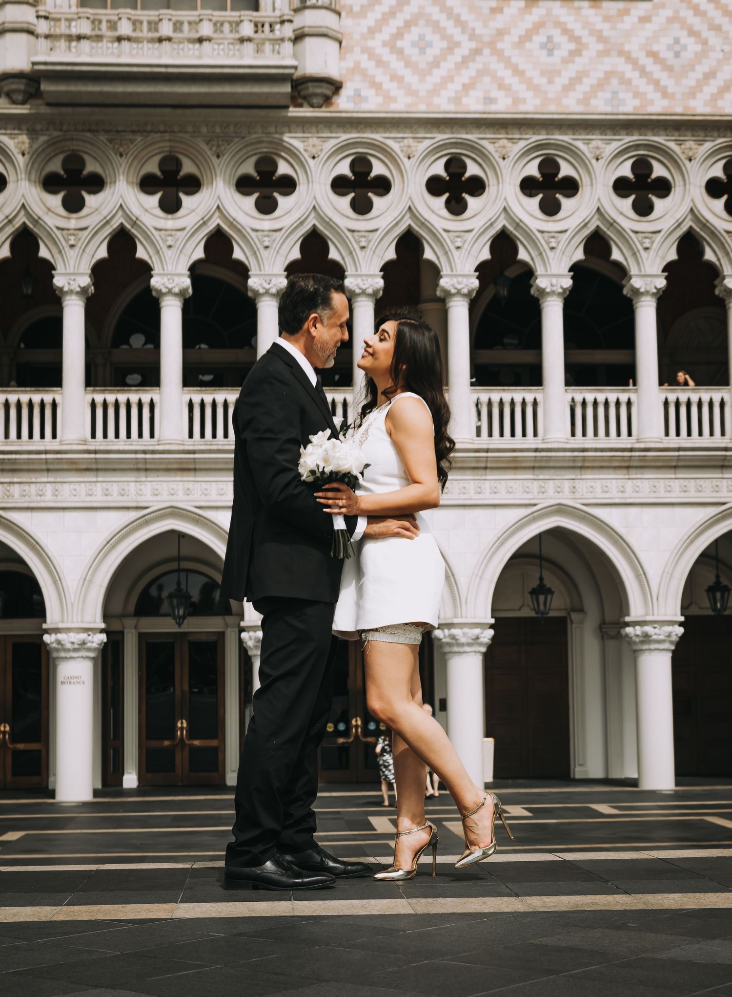Bride and groom sharing intimate moment with bouquet before Gothic Venetian architecture in Las Vegas.