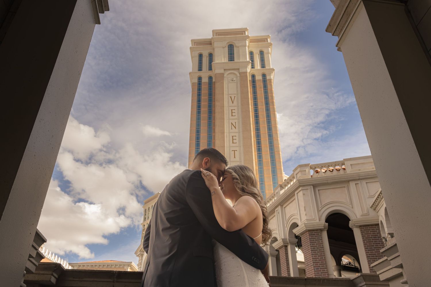 Newlyweds kissing beneath the towering Venetian Resort Las Vegas under dramatic cloudy skies.