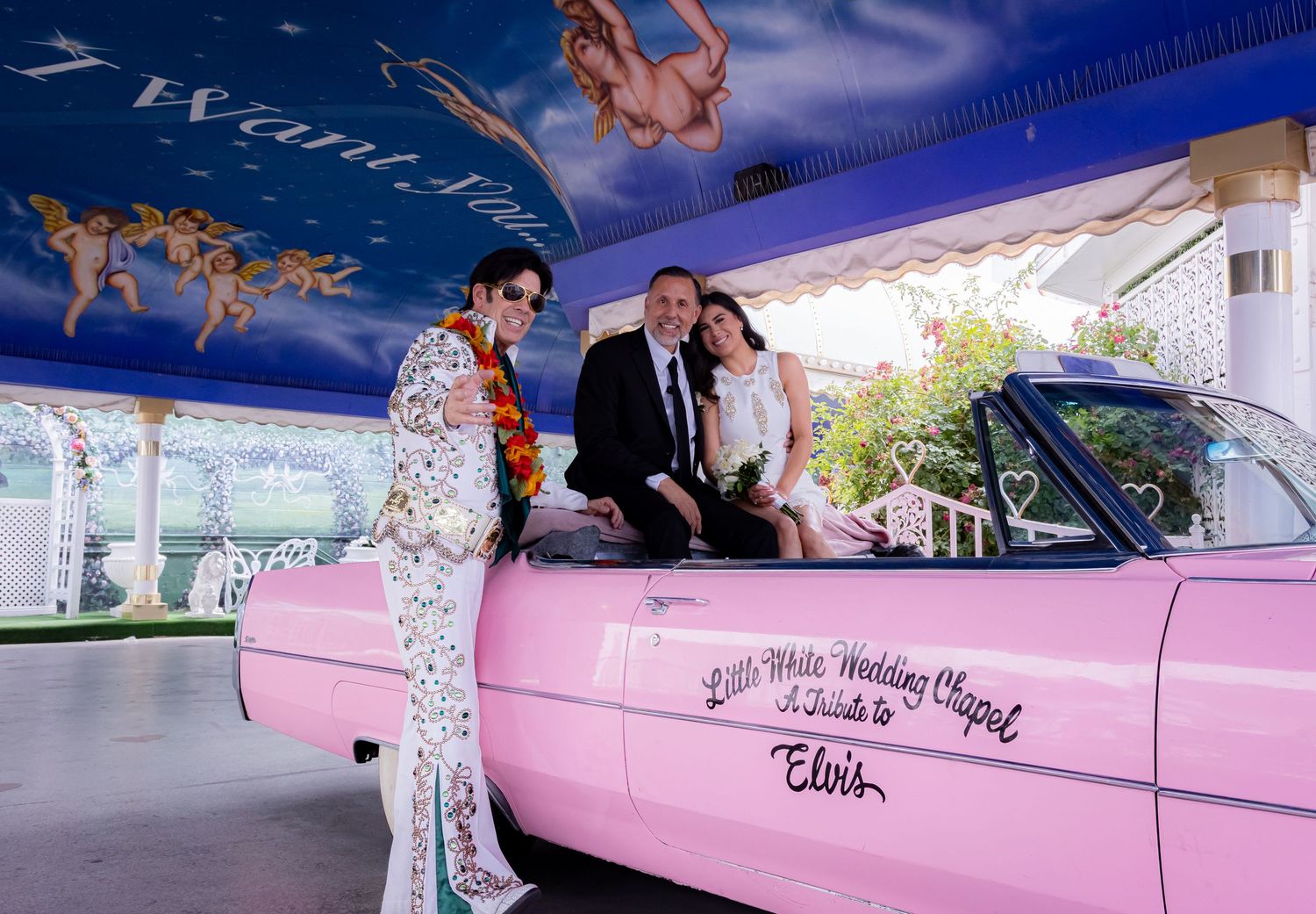 Couple posing with Elvis impersonator beside a pink Cadillac at Little White Wedding Chapel.