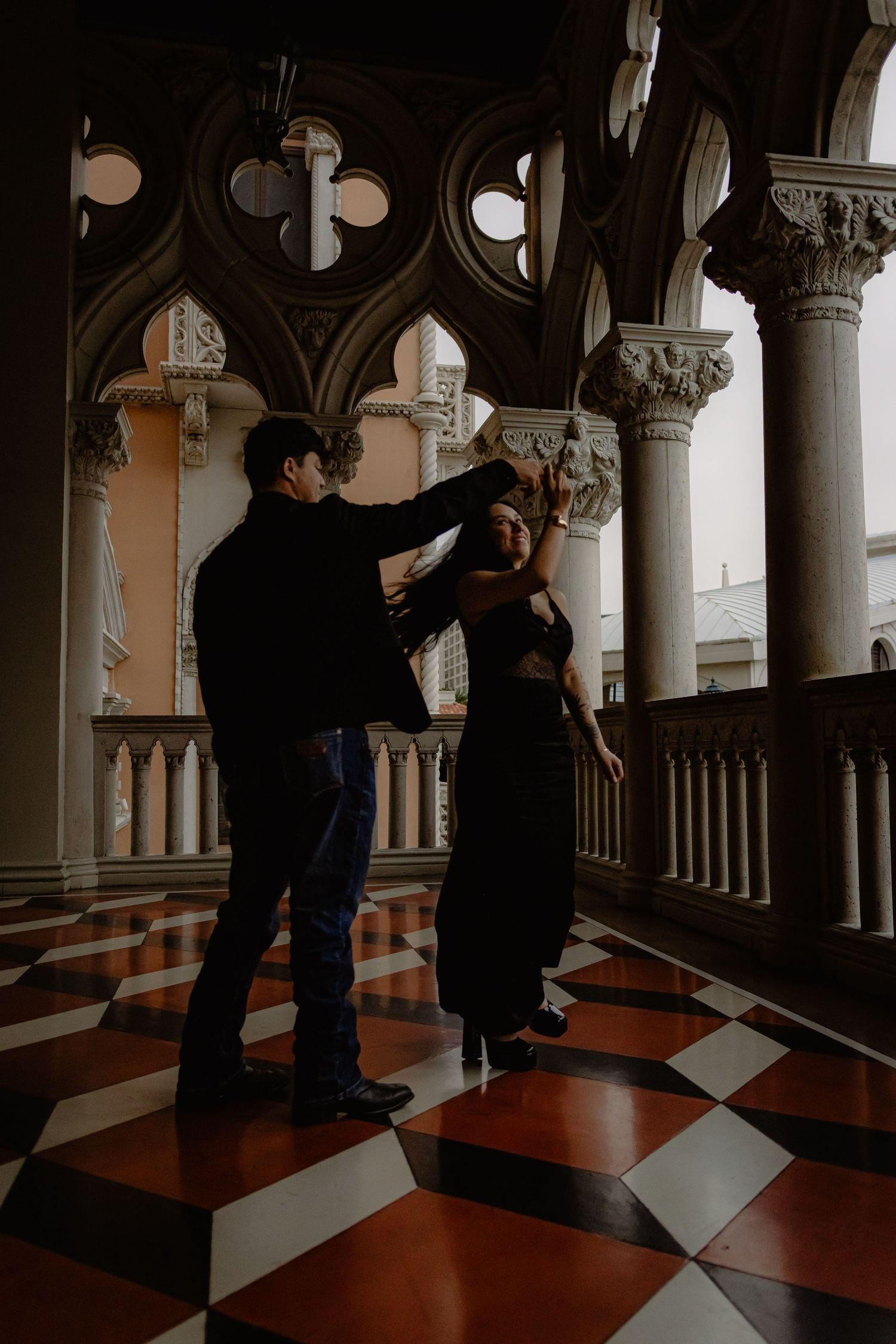 Couple dancing together in a grand Gothic-arched corridor with ornate columns and red checkered marble floors.