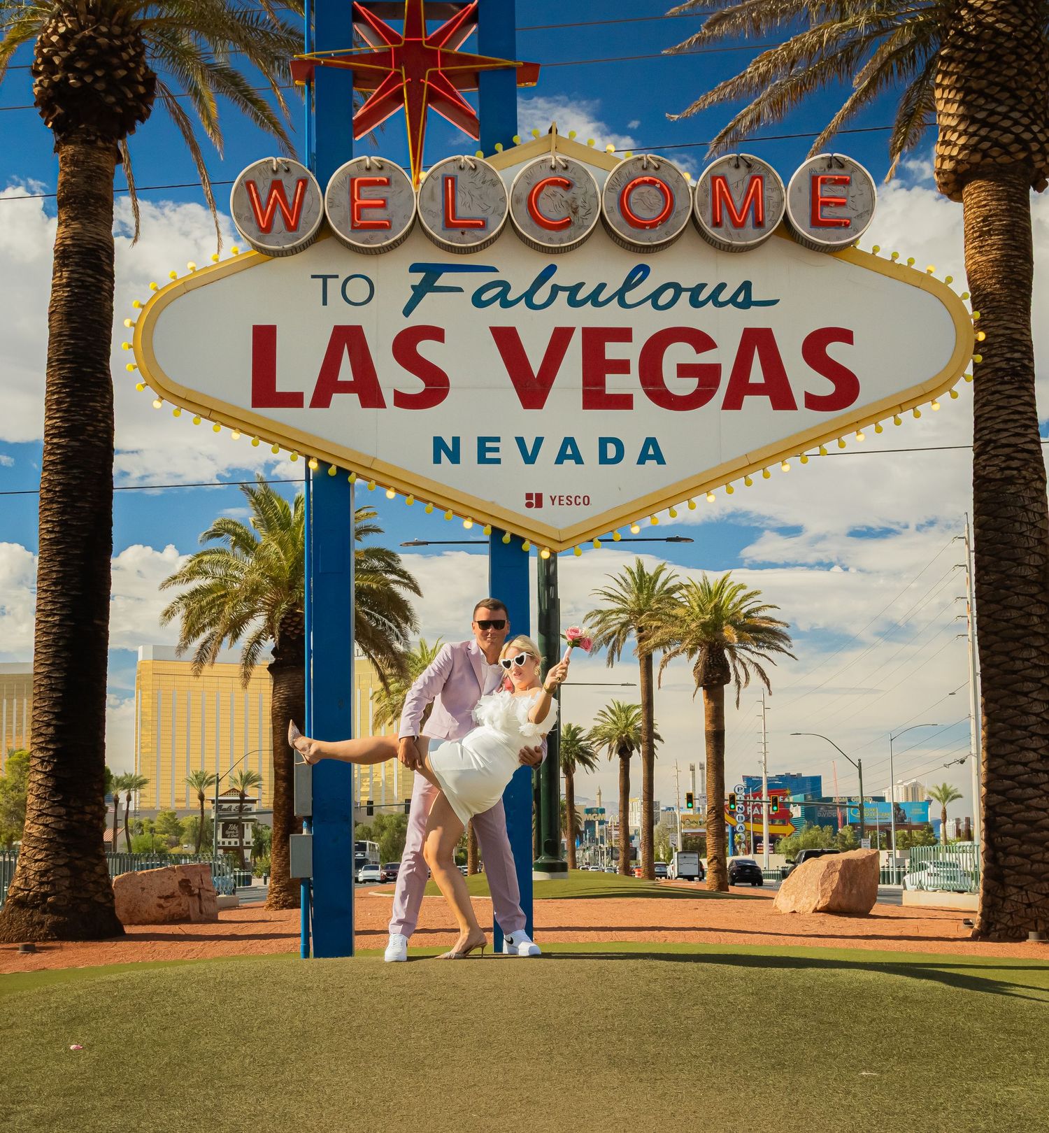 Happy couple posing playfully under the iconic Welcome to Fabulous Las Vegas Nevada sign with palm trees.