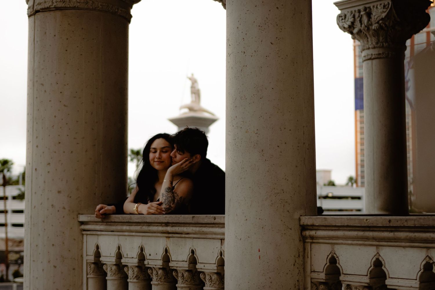 Couple sharing a tender kiss between ornate columns on a balcony at The Venetian Las Vegas.