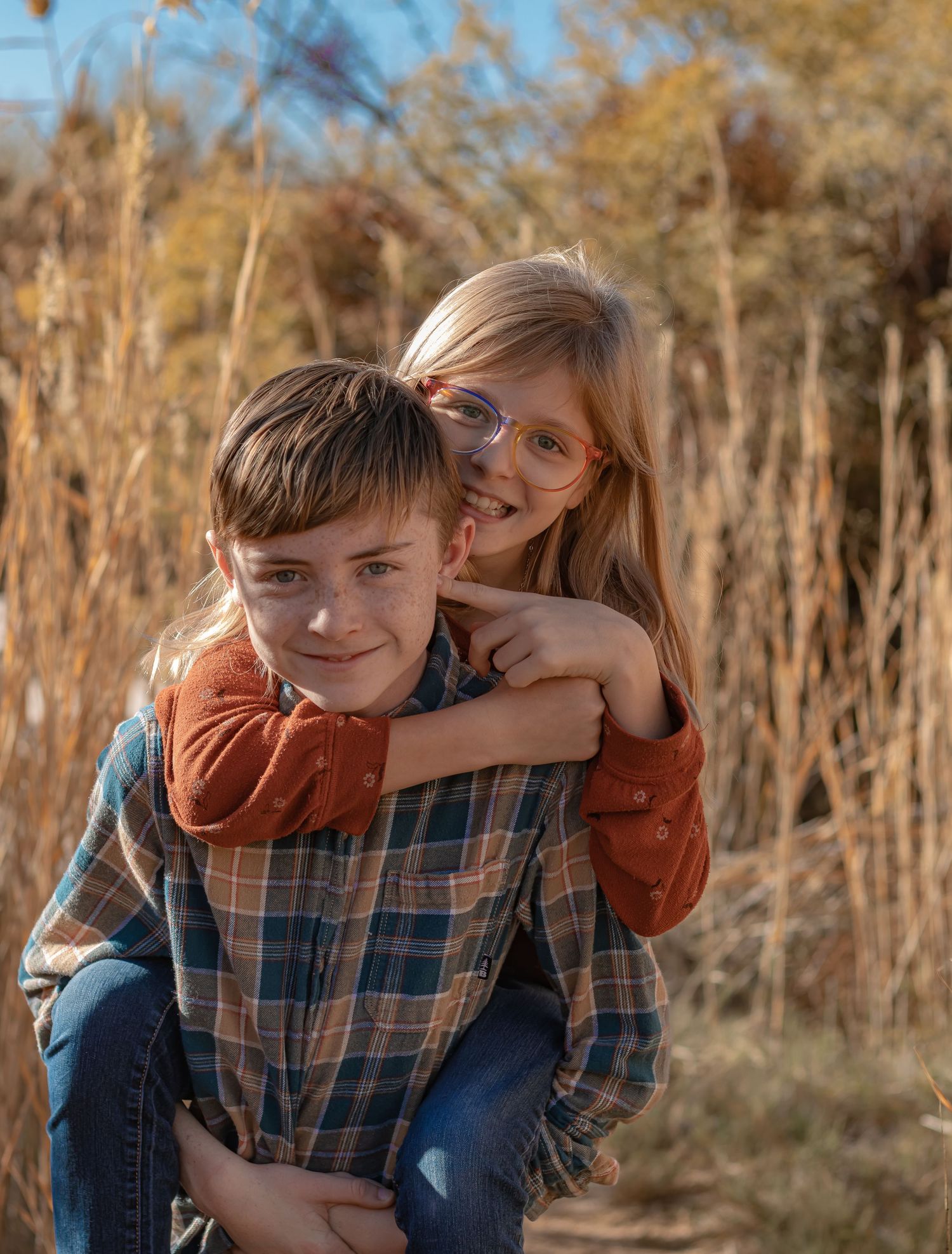 A smiling boy gives a laughing girl a piggyback ride in a golden autumn field.