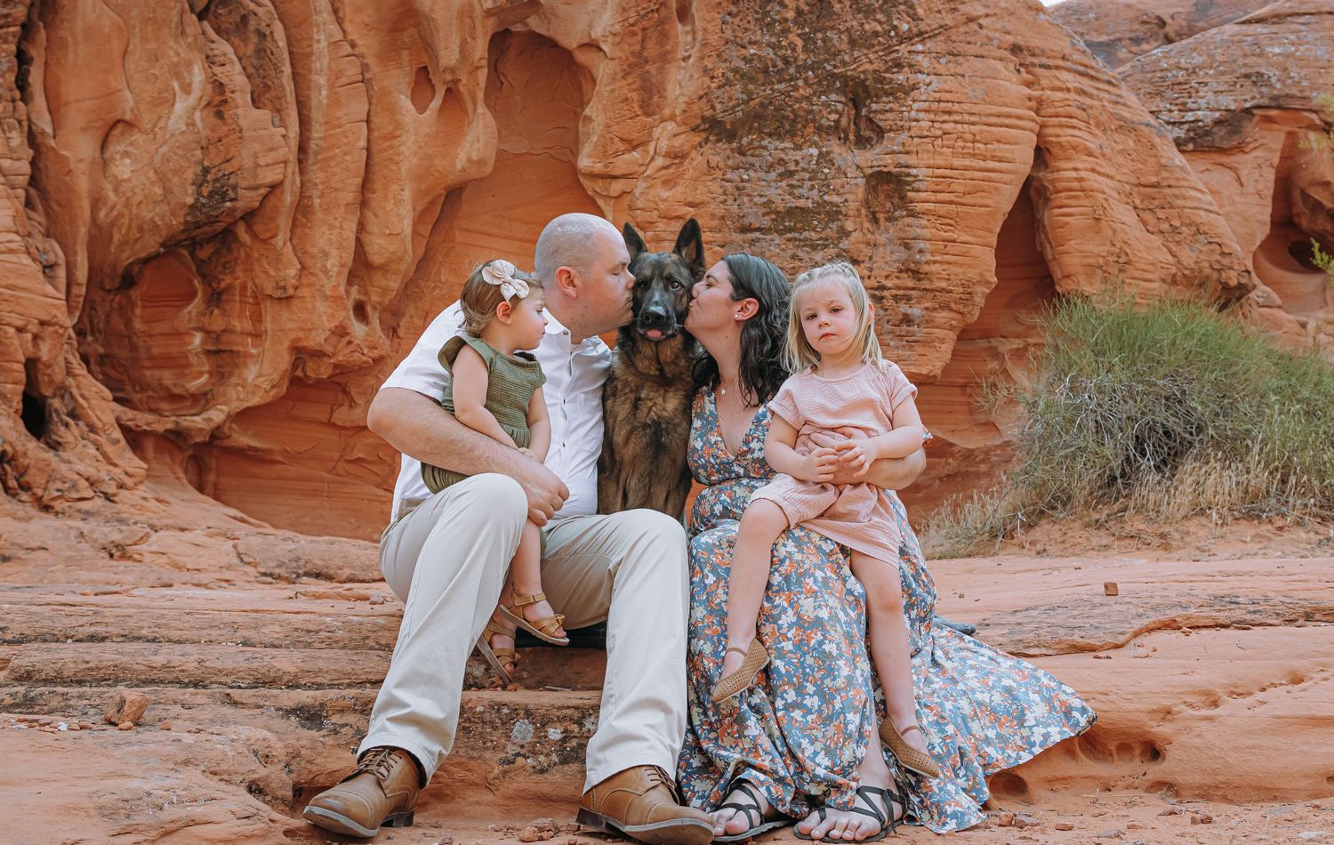 Family with two children and a German Shepherd dog pose among red rock formations outdoors.