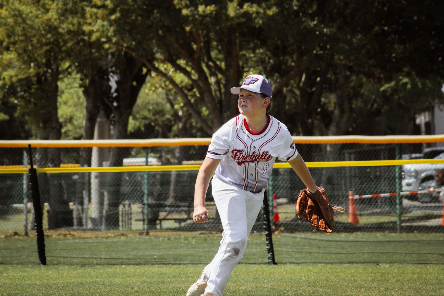 Young baseball player in white Fireballs uniform fields ball on sunny green outfield grass. sports and touramnets